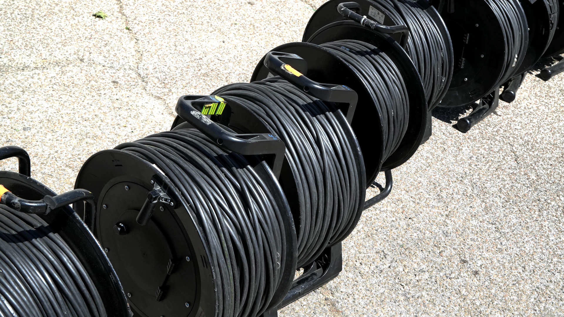 Several large spools of black cable on a concrete surface.