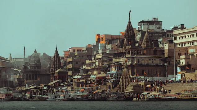 Ancient buildings and temples line a riverbank with boats.