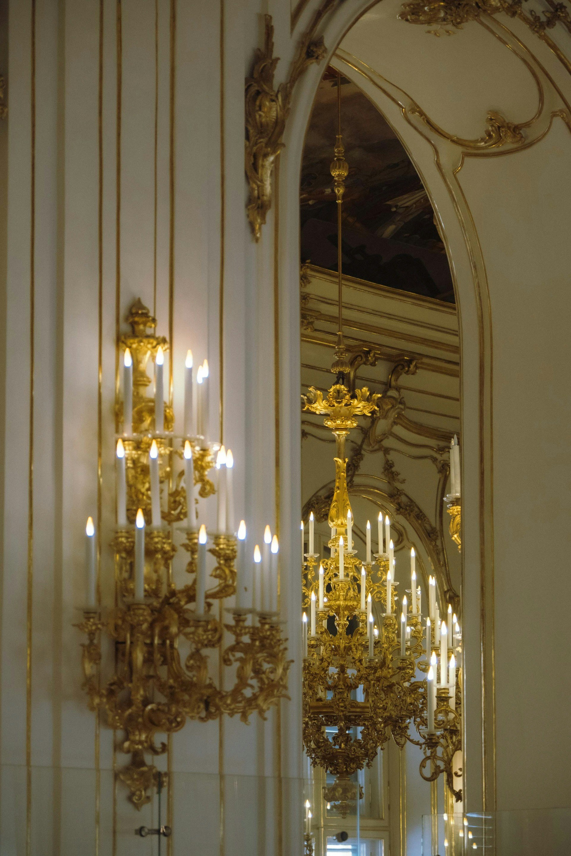 Ornamentados candelabros dourados e lustres em um grande salão.