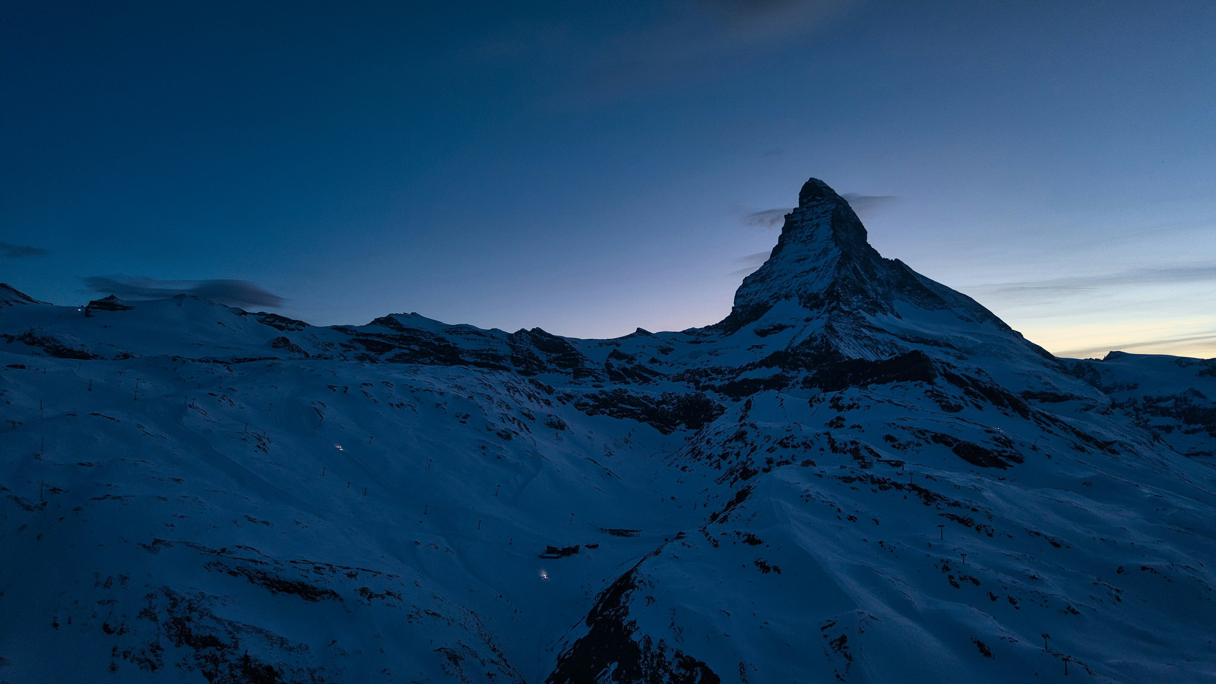 Snowy mountain peak under a dark blue twilight sky.