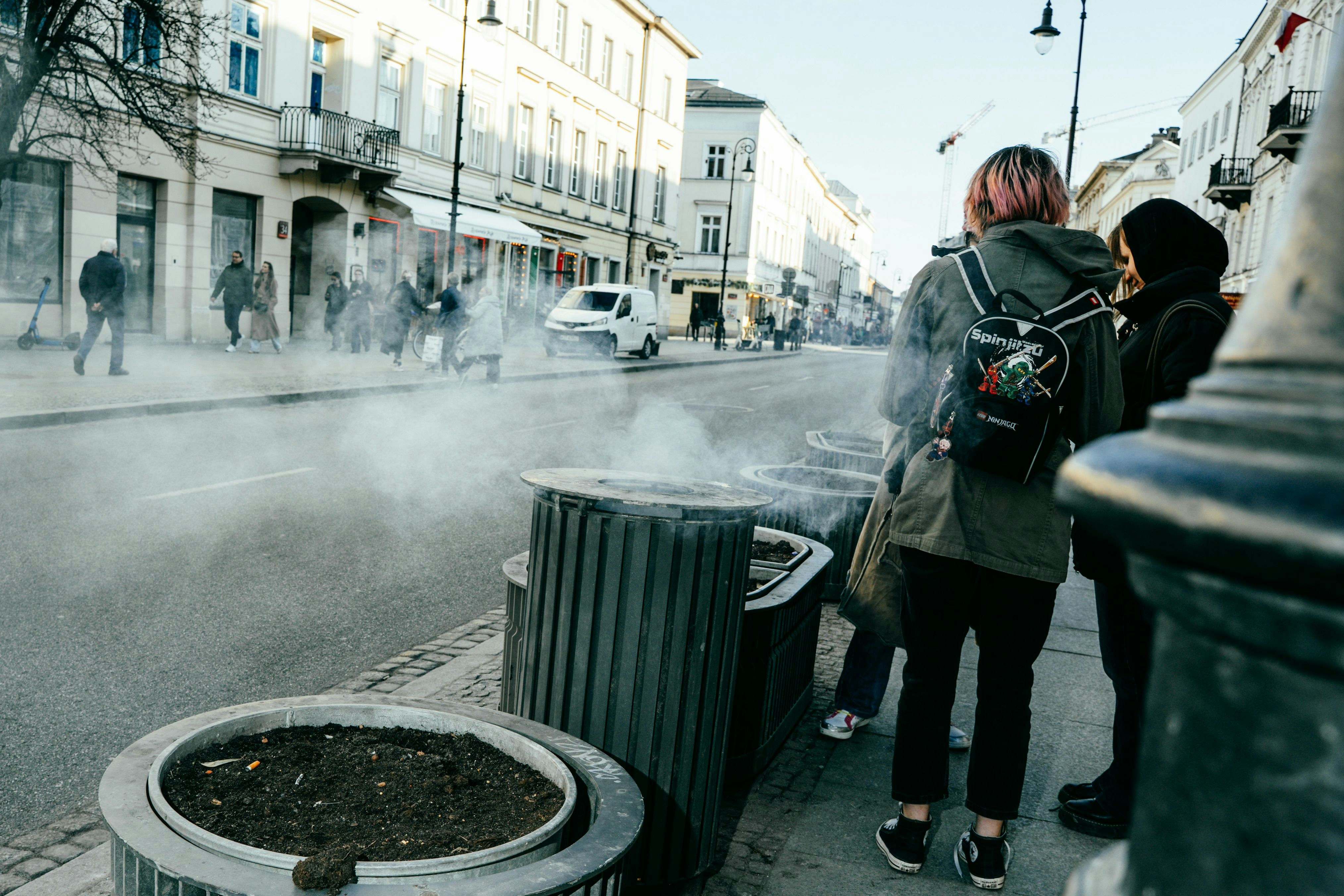 La gente está de pie en una calle con vapor saliendo de los contenedores.
