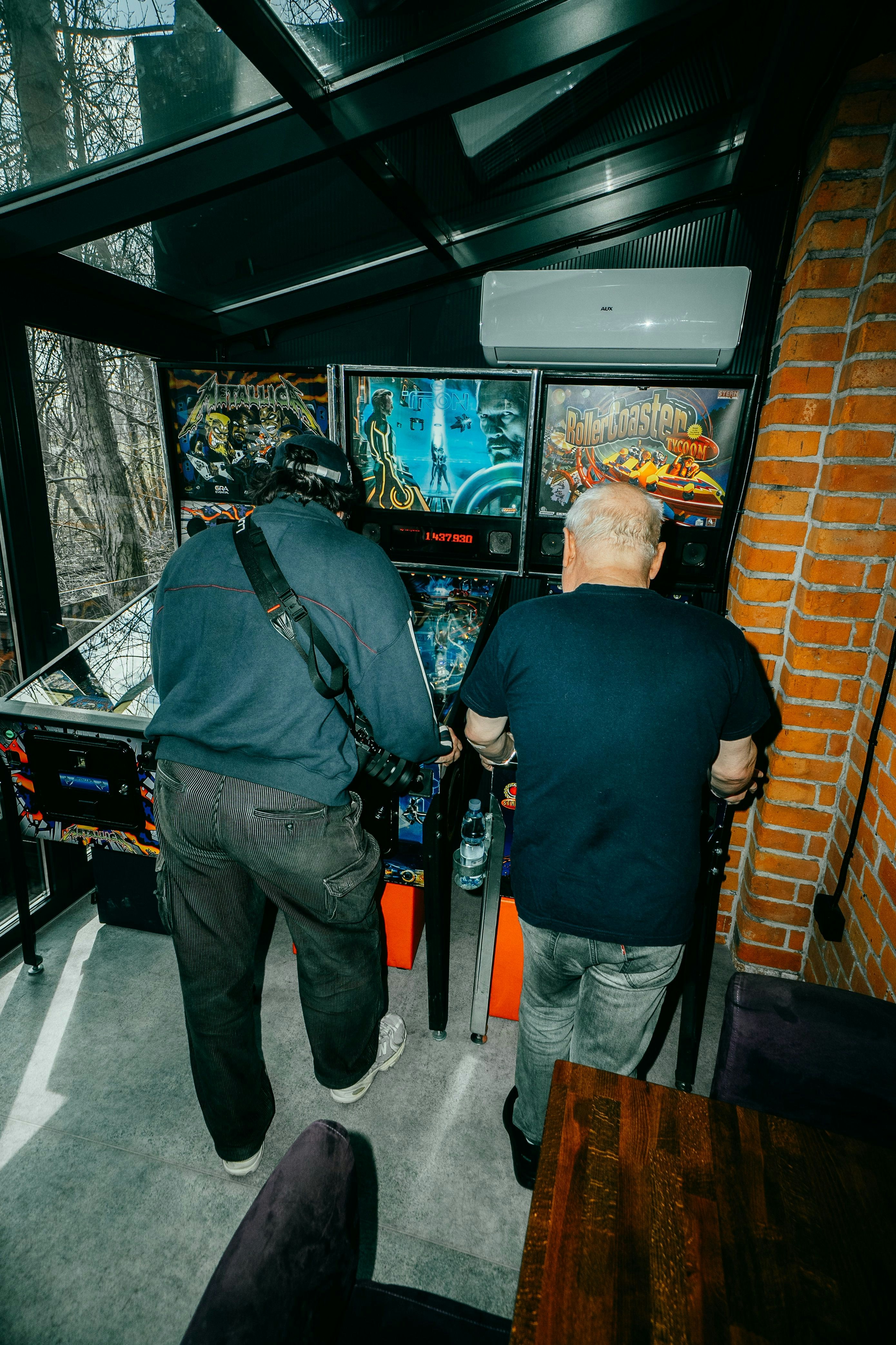 Two men playing pinball machines indoors