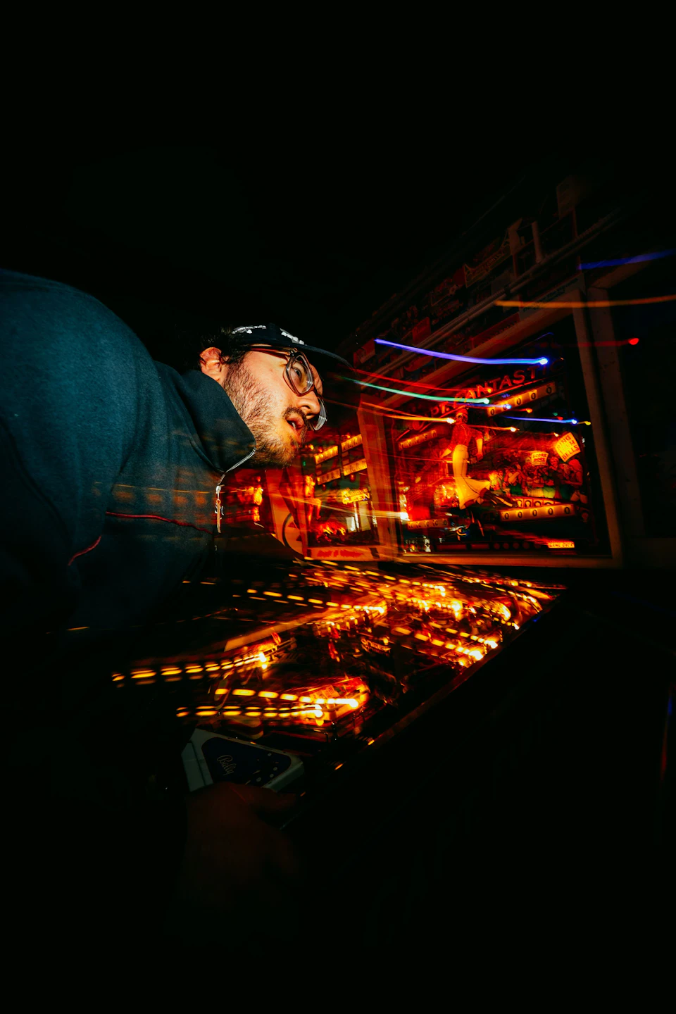 Man stands in front of TV screen displaying colorful lights while wearing glasses and jacket