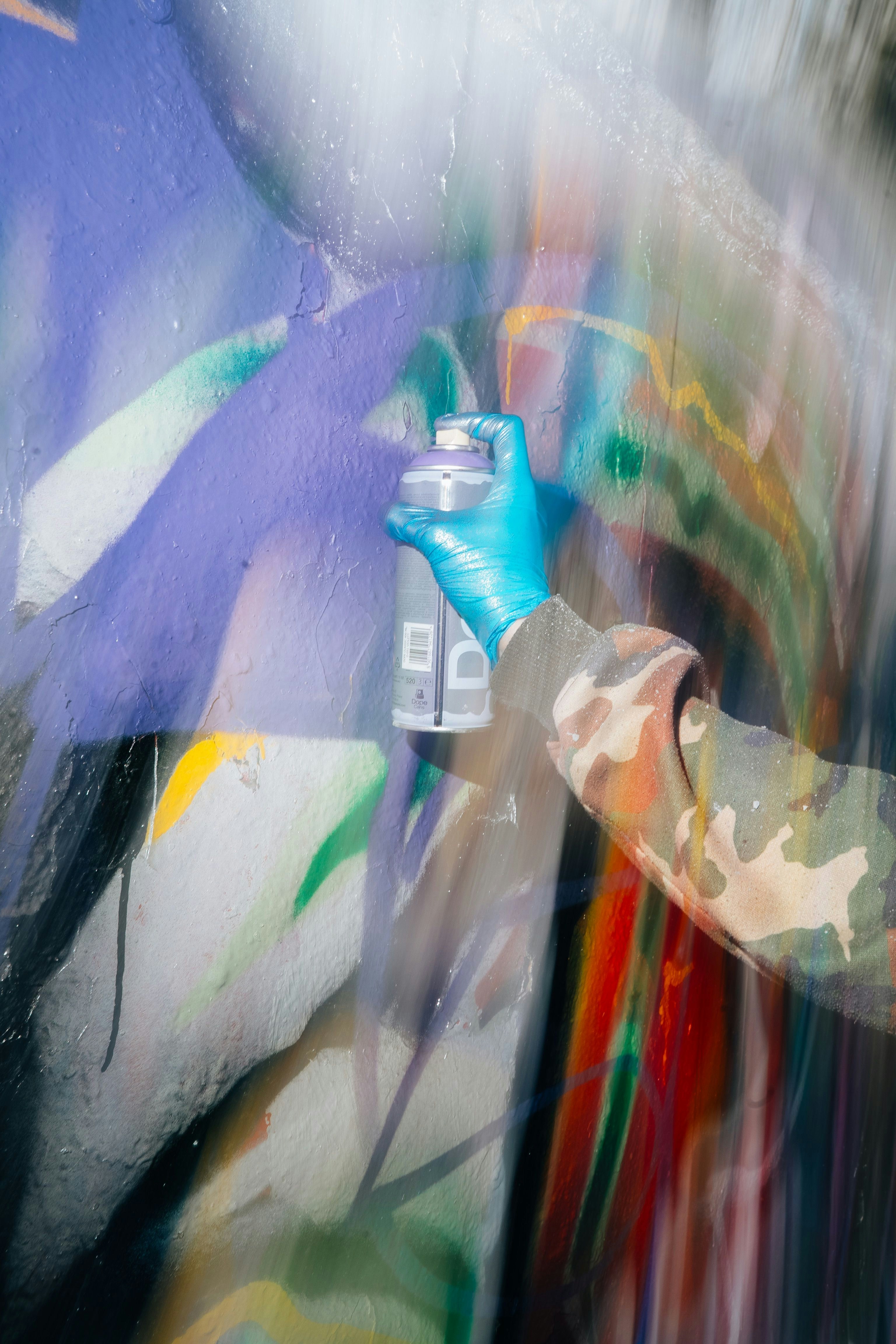 Hand in glove spraying colorful paint on wall