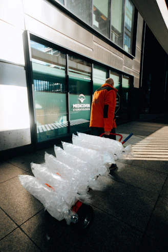 Man in orange jacket pulling large bags on cart