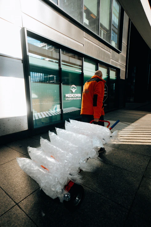 Man in orange jacket pulling large bags on cart