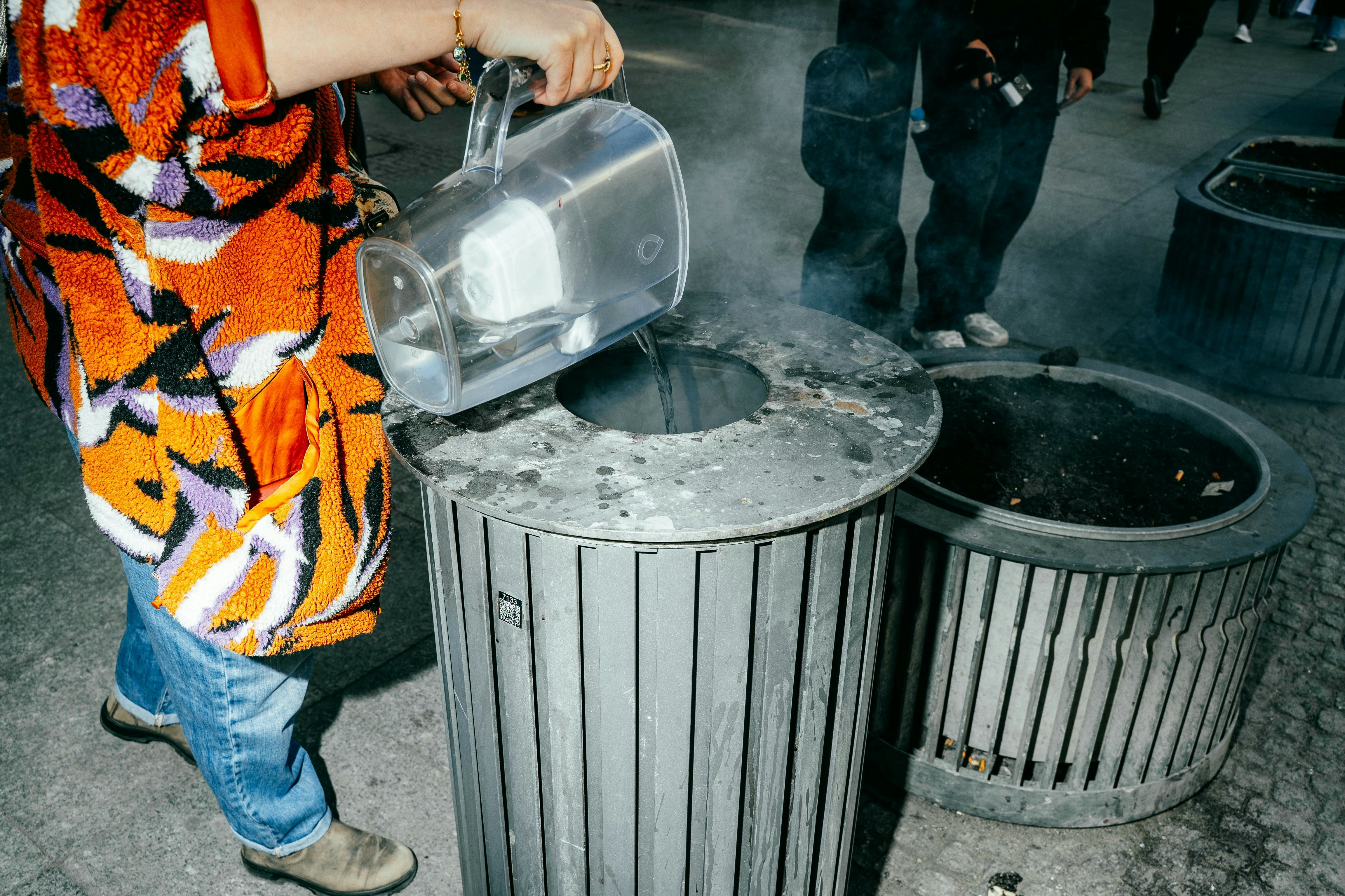 Persona vertiendo líquido en un cubo de basura.