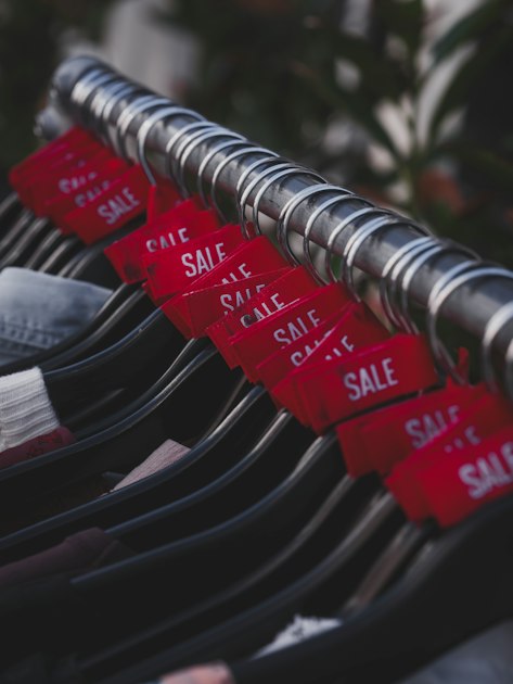 A row of clothes on black hangers on a metal rail, each with a red tag reading SALE