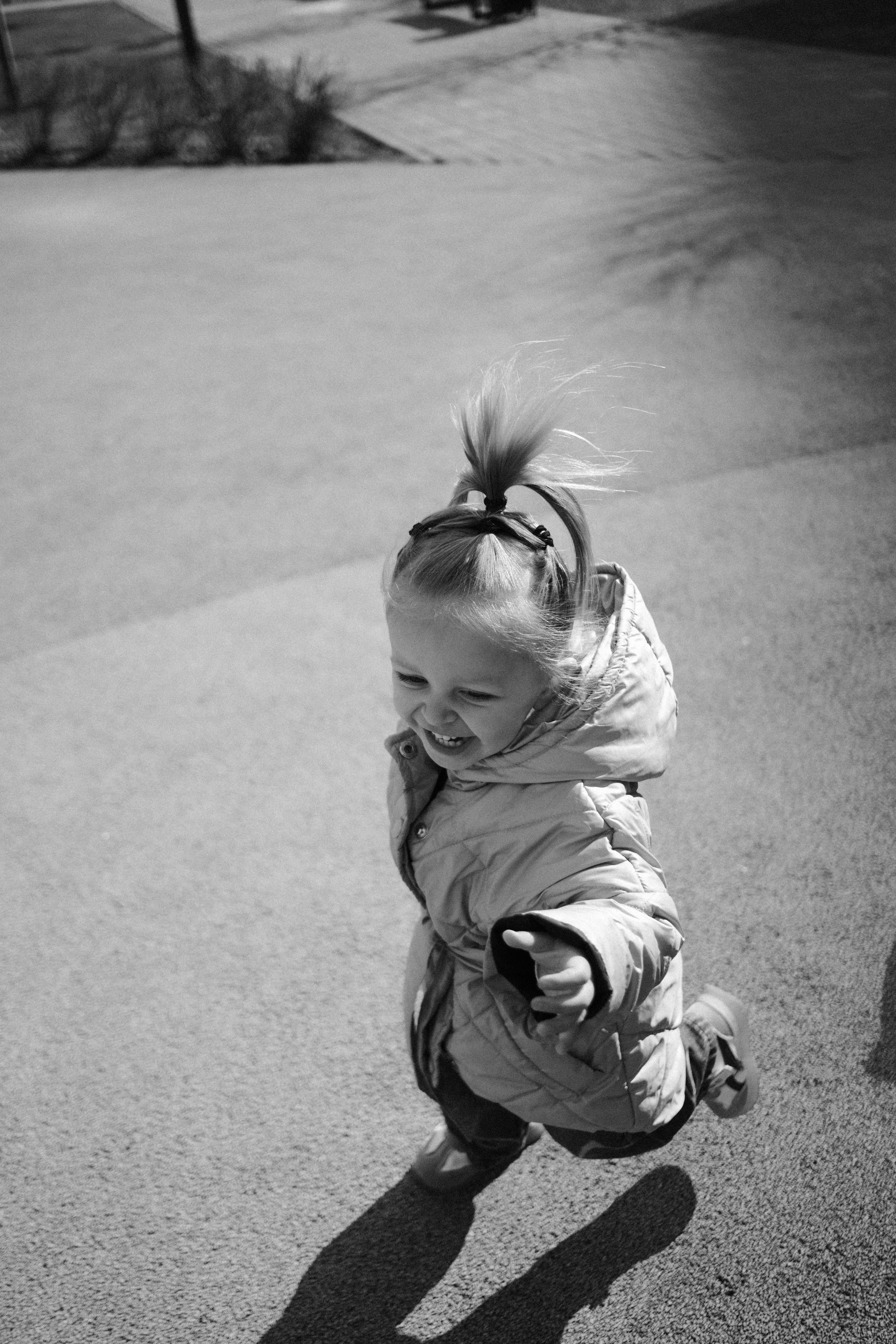 A happy toddler running outdoors in black and white.