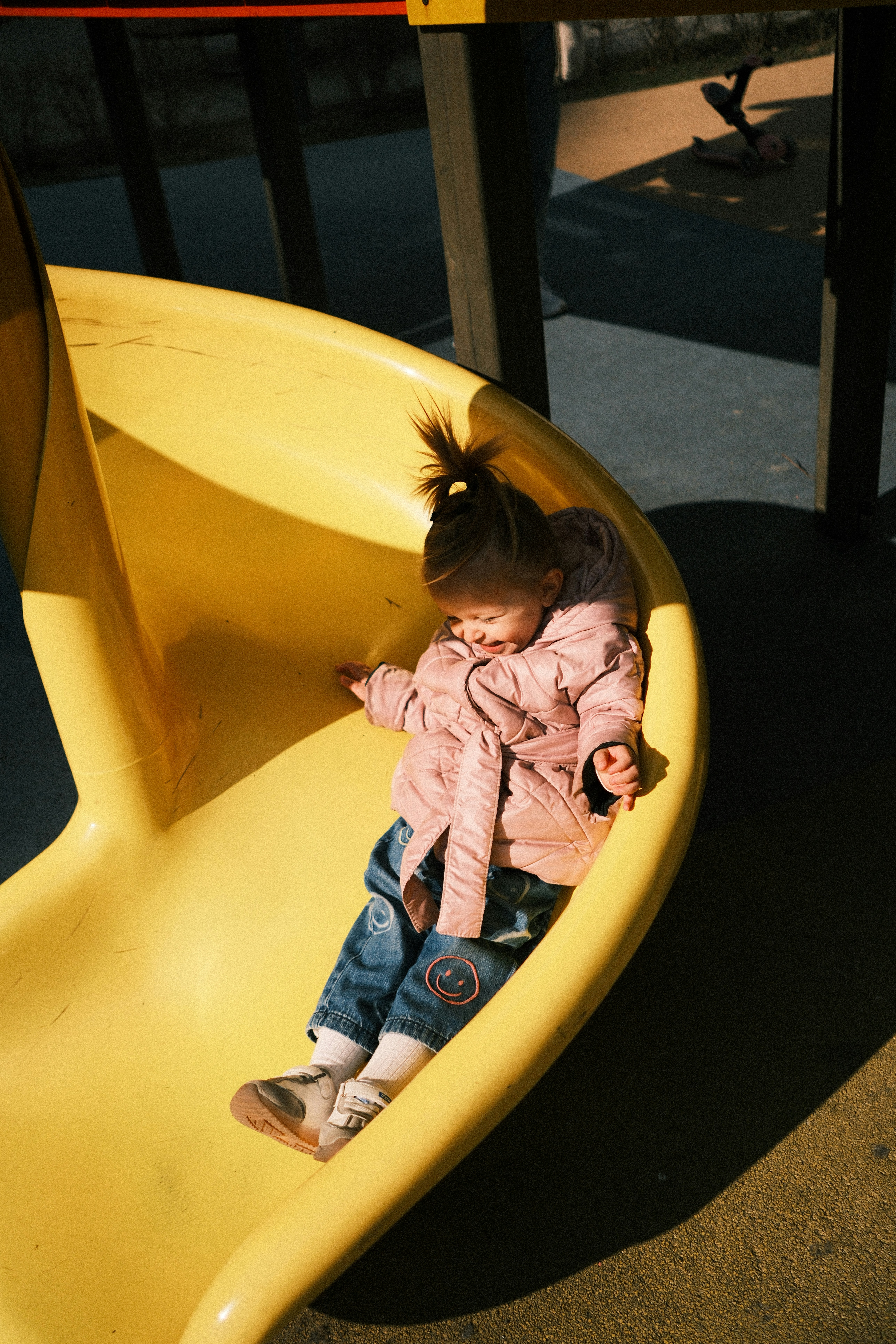 A young child sits on a yellow playground slide.