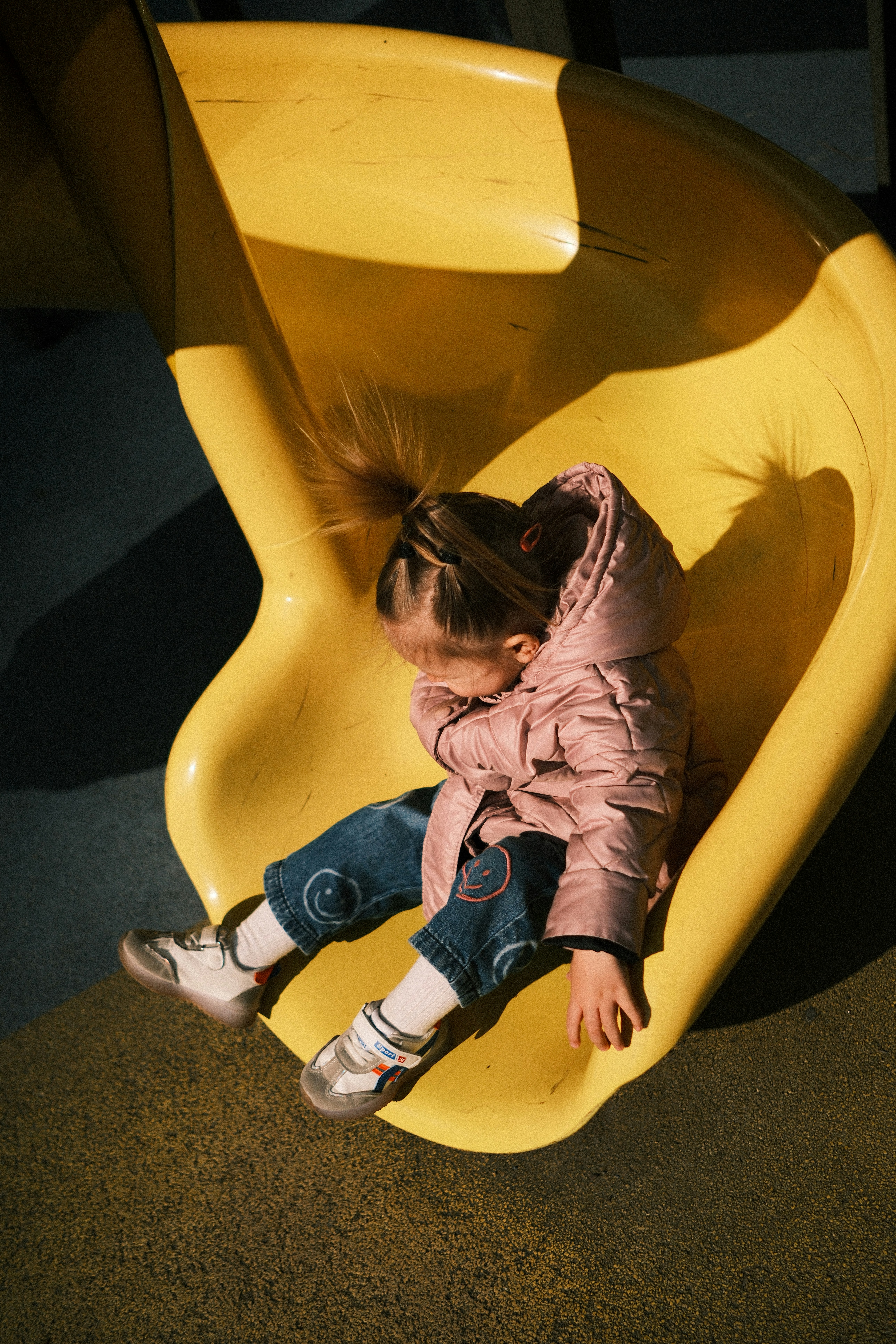 Young girl sliding down a yellow playground slide
