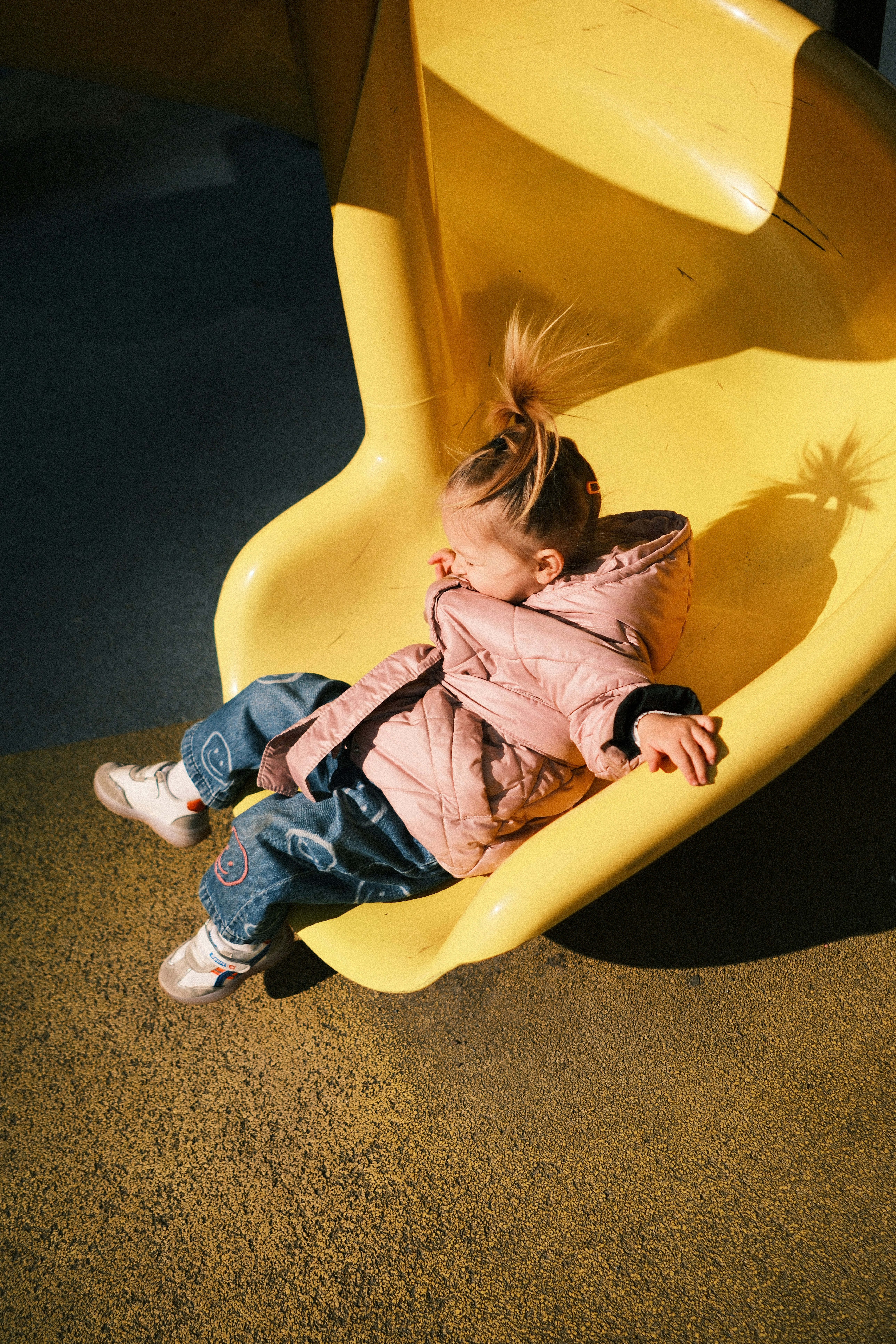 Young girl sliding down a yellow playground slide