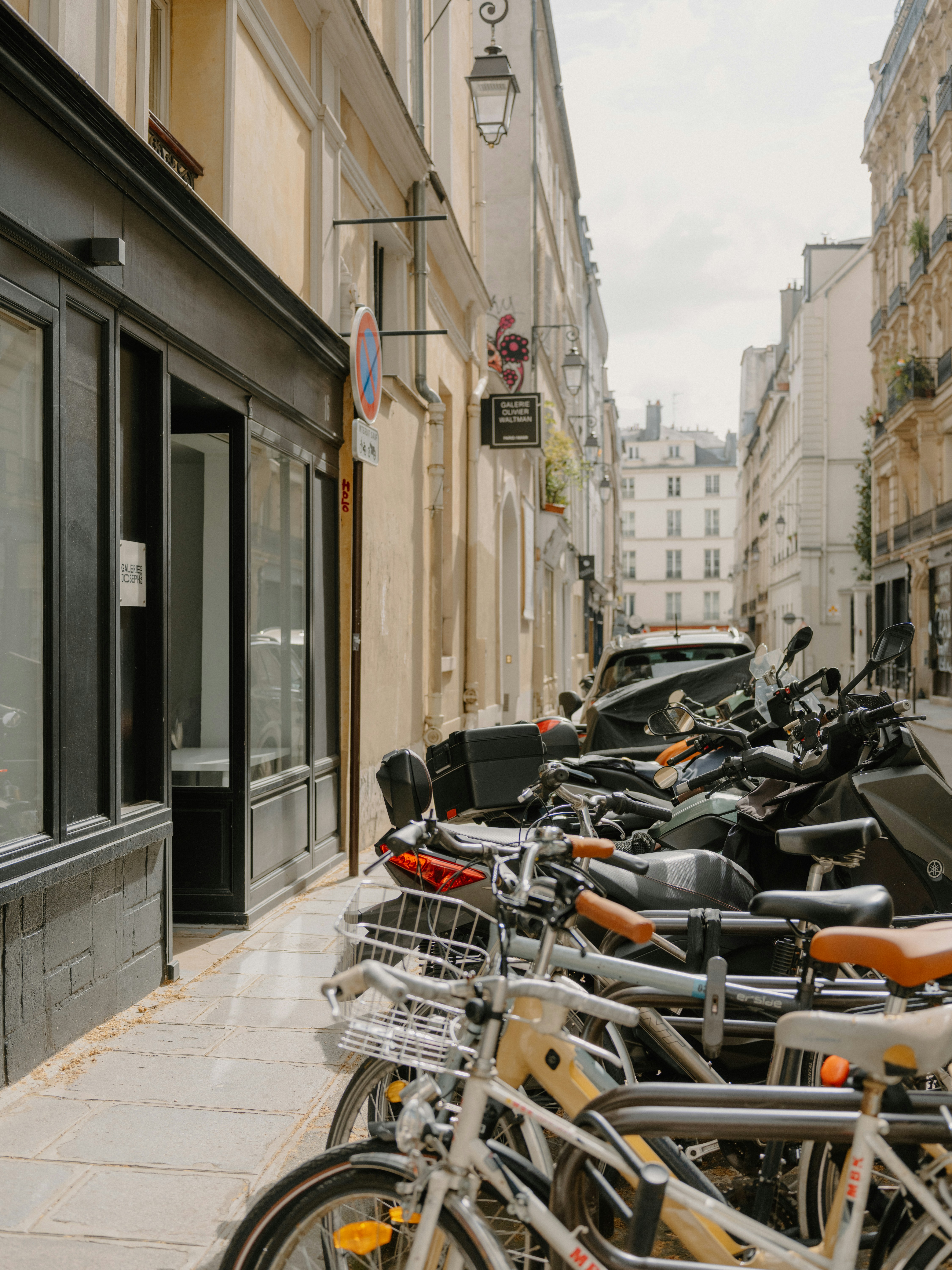 Parked bicycles and scooters line a narrow street.