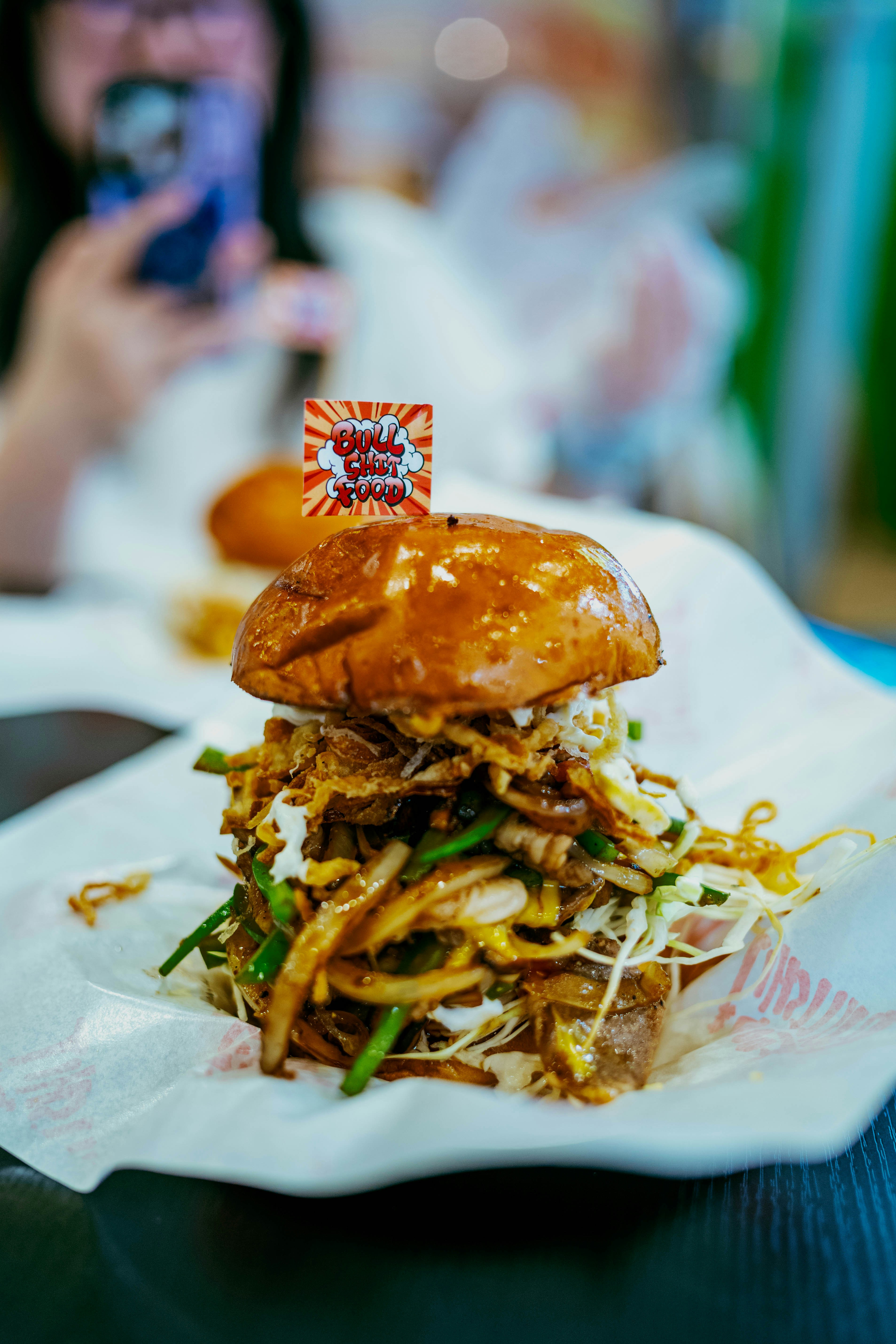 Un hamburger alto, riempito, con condimenti croccanti e una bandiera.