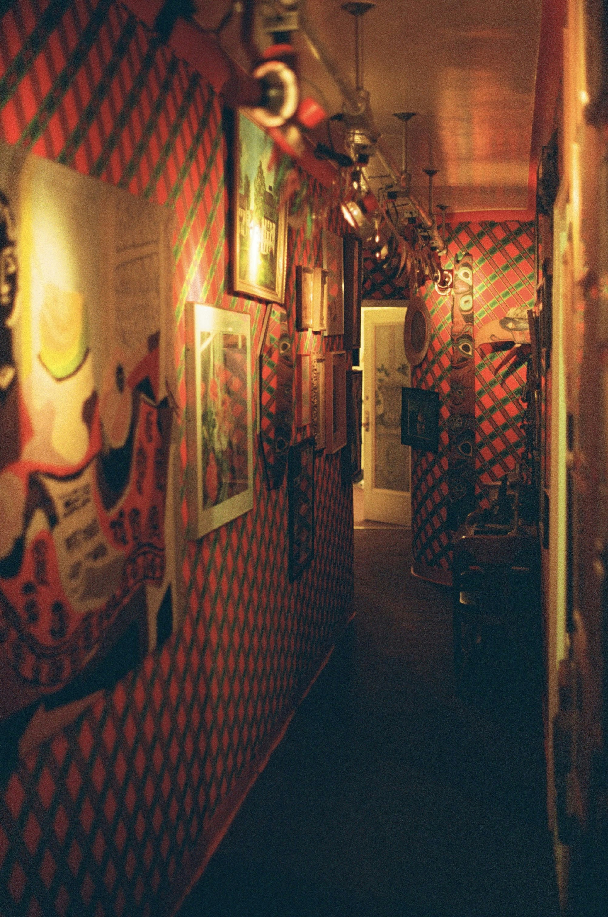 Hallway with red diamond patterned wallpaper and framed art.