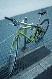 A green bicycle locked to a pole on a sidewalk.