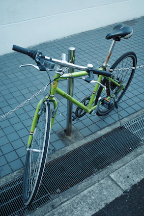 A green bicycle locked to a pole on a sidewalk.