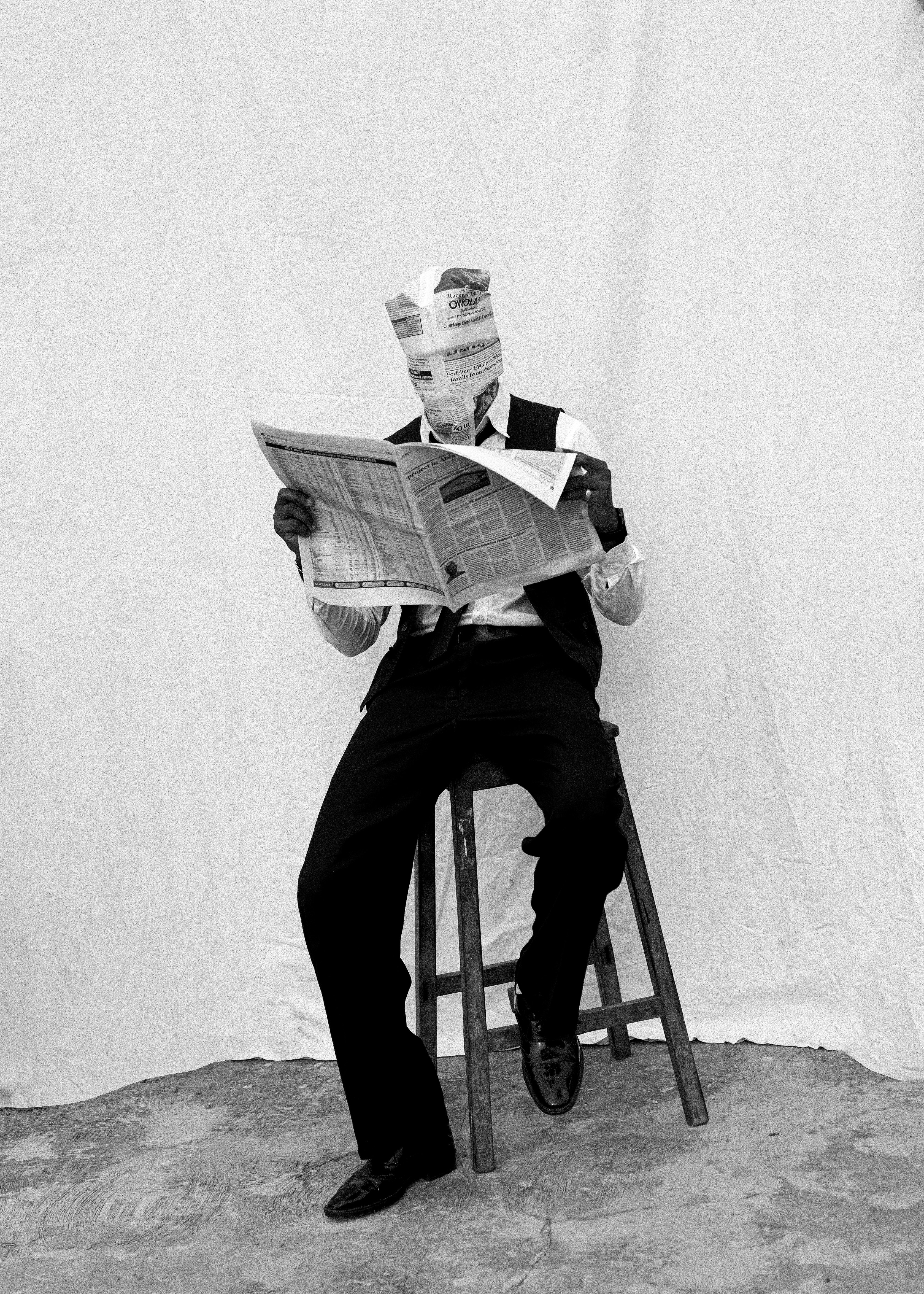 Man wearing a newspaper hat reads a newspaper