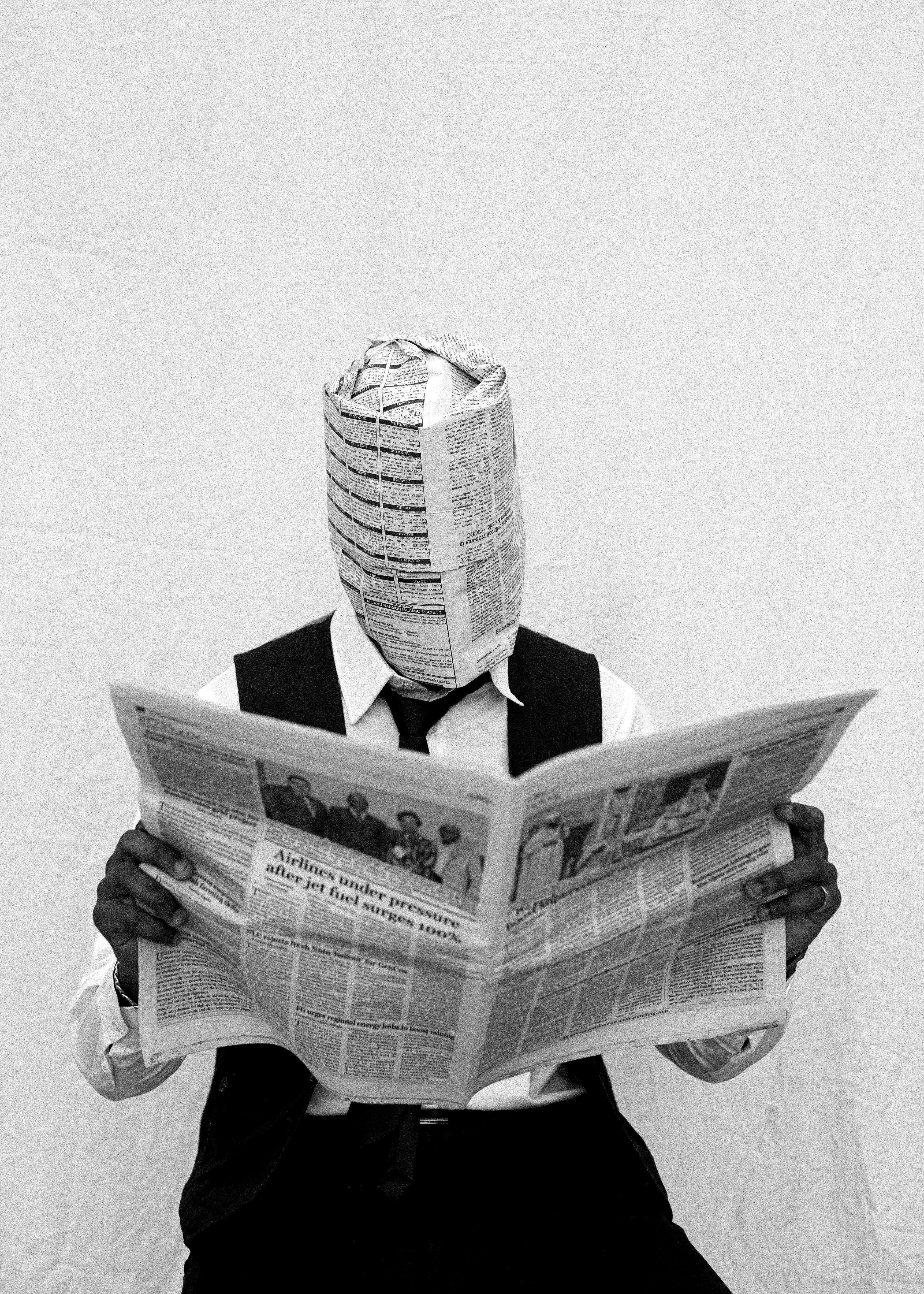 Person with newspaper covering face reads news