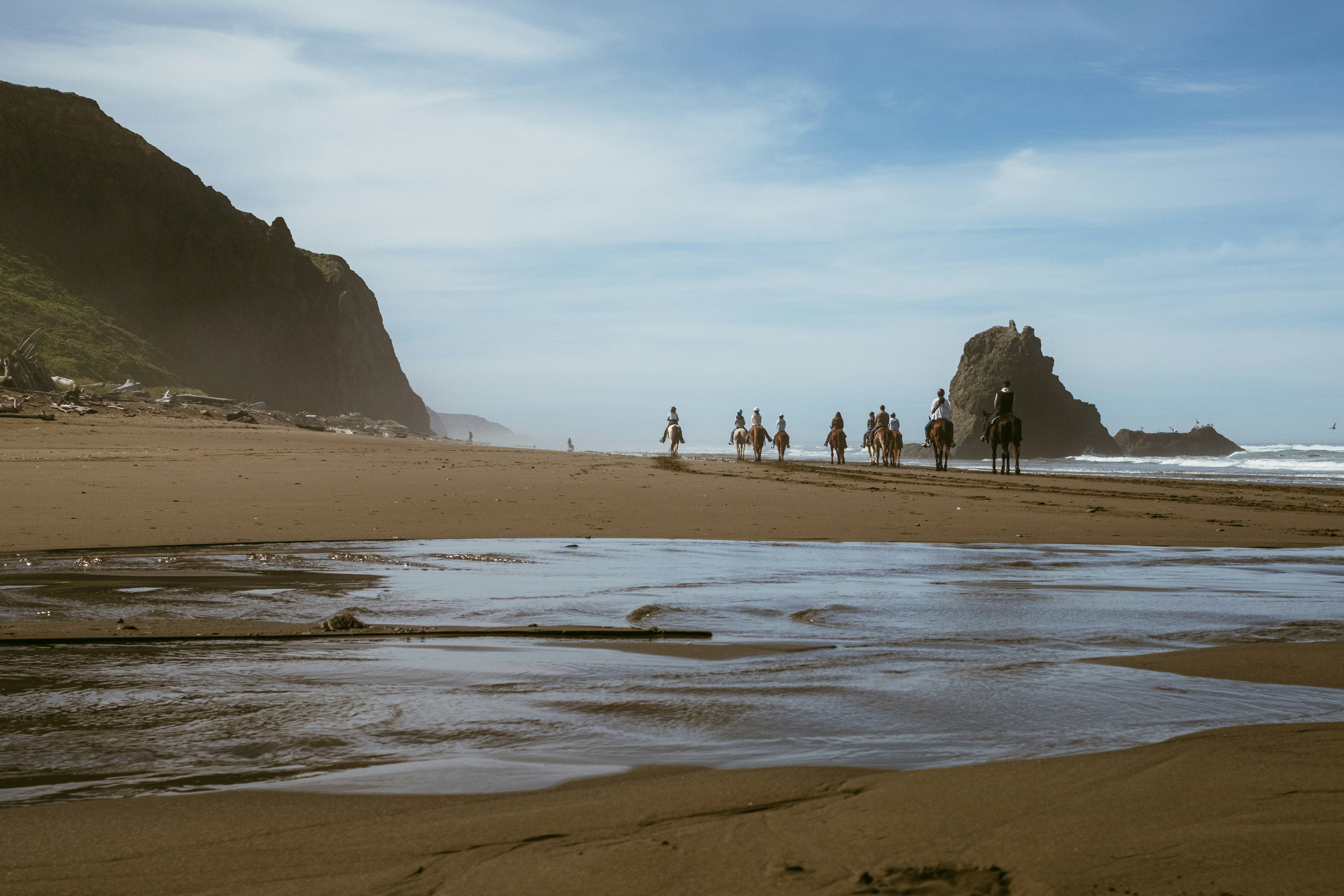 People on horseback ride along a sandy beach.