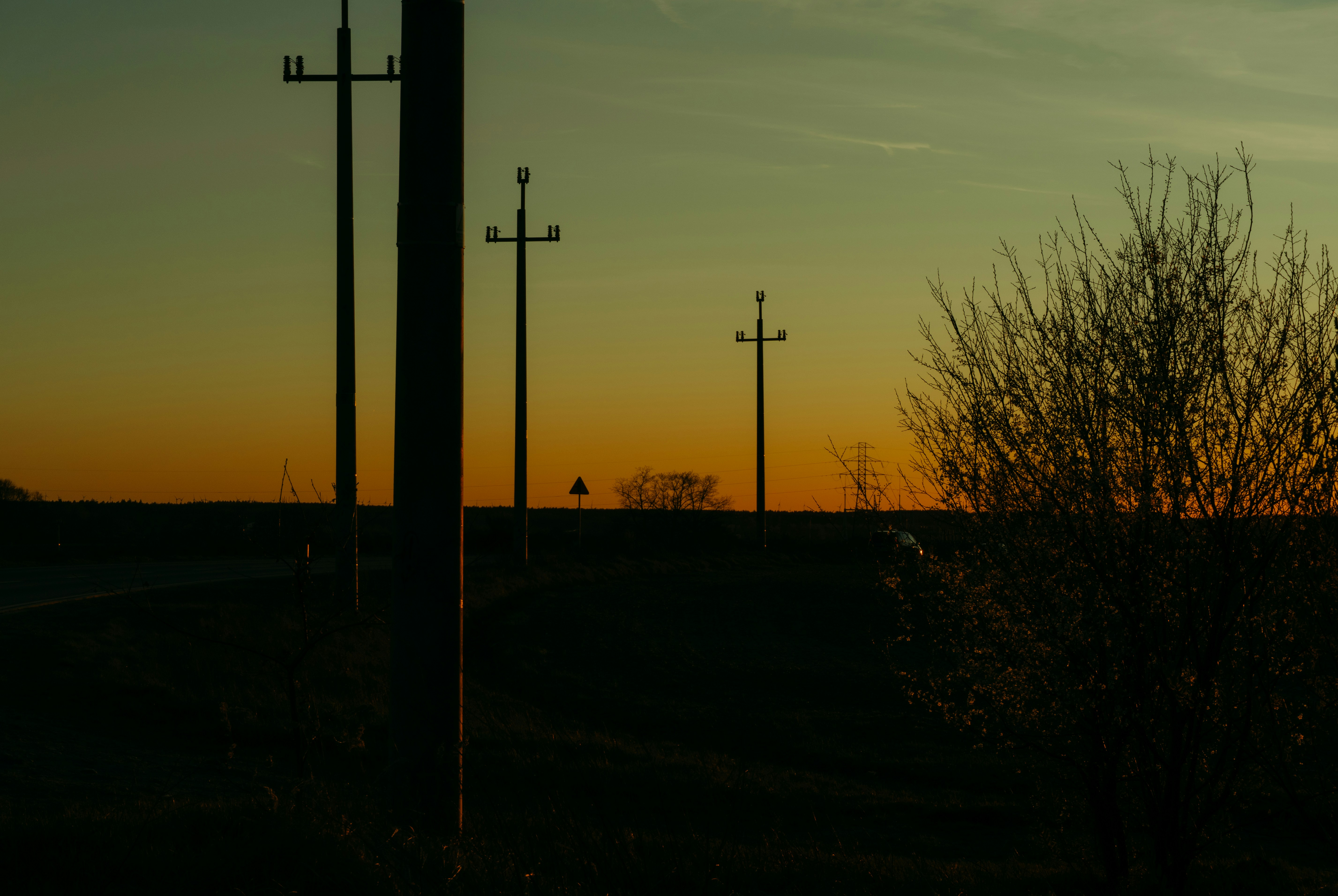 Telephone poles line a rural road at sunset