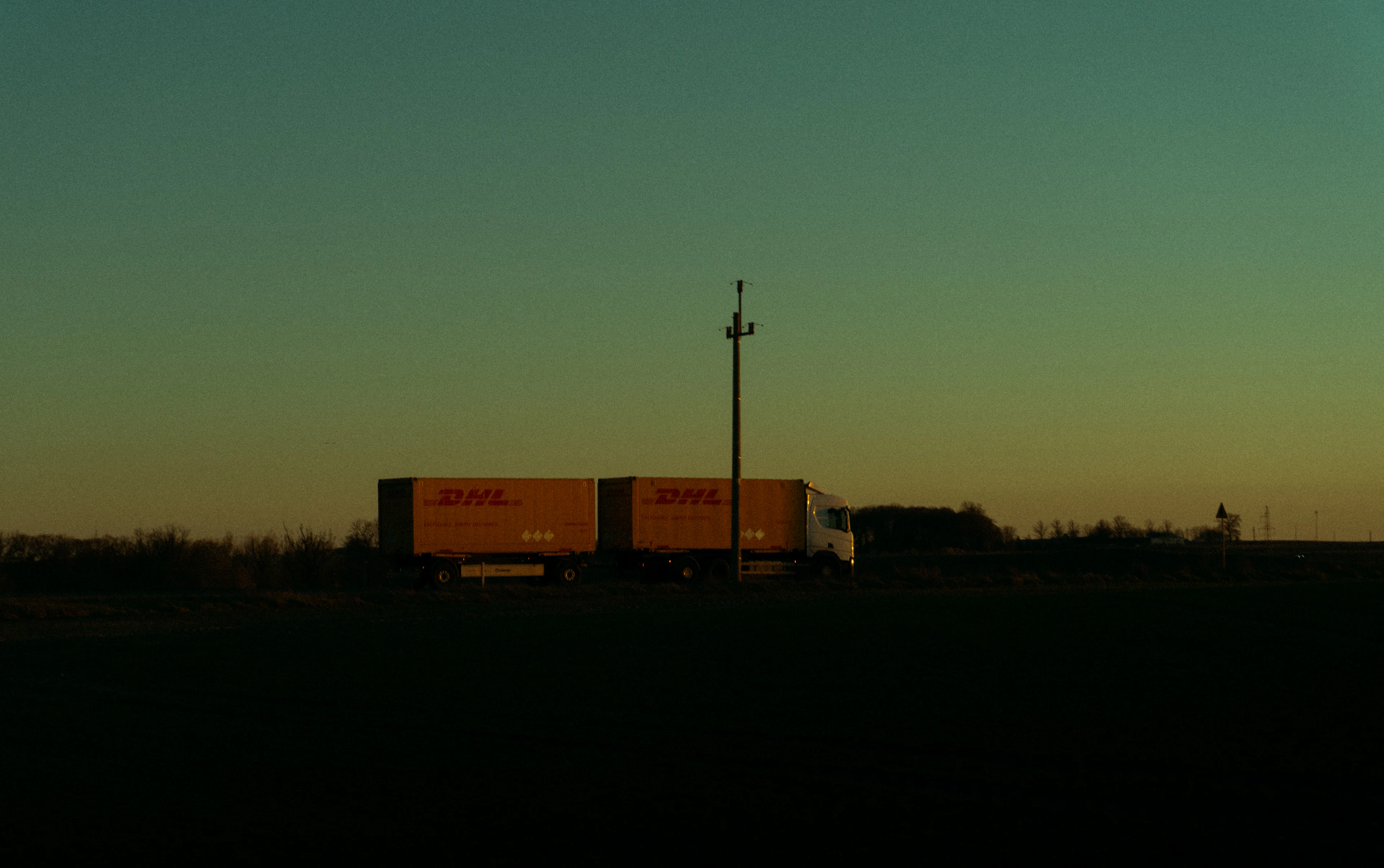 A semi-truck silhouetted on the horizon against a twilight sky