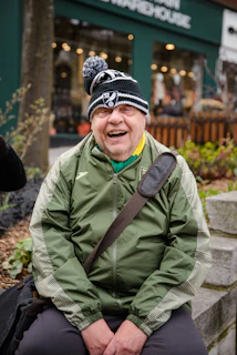 Un homme âgé, portant un chapeau et une veste, rit.