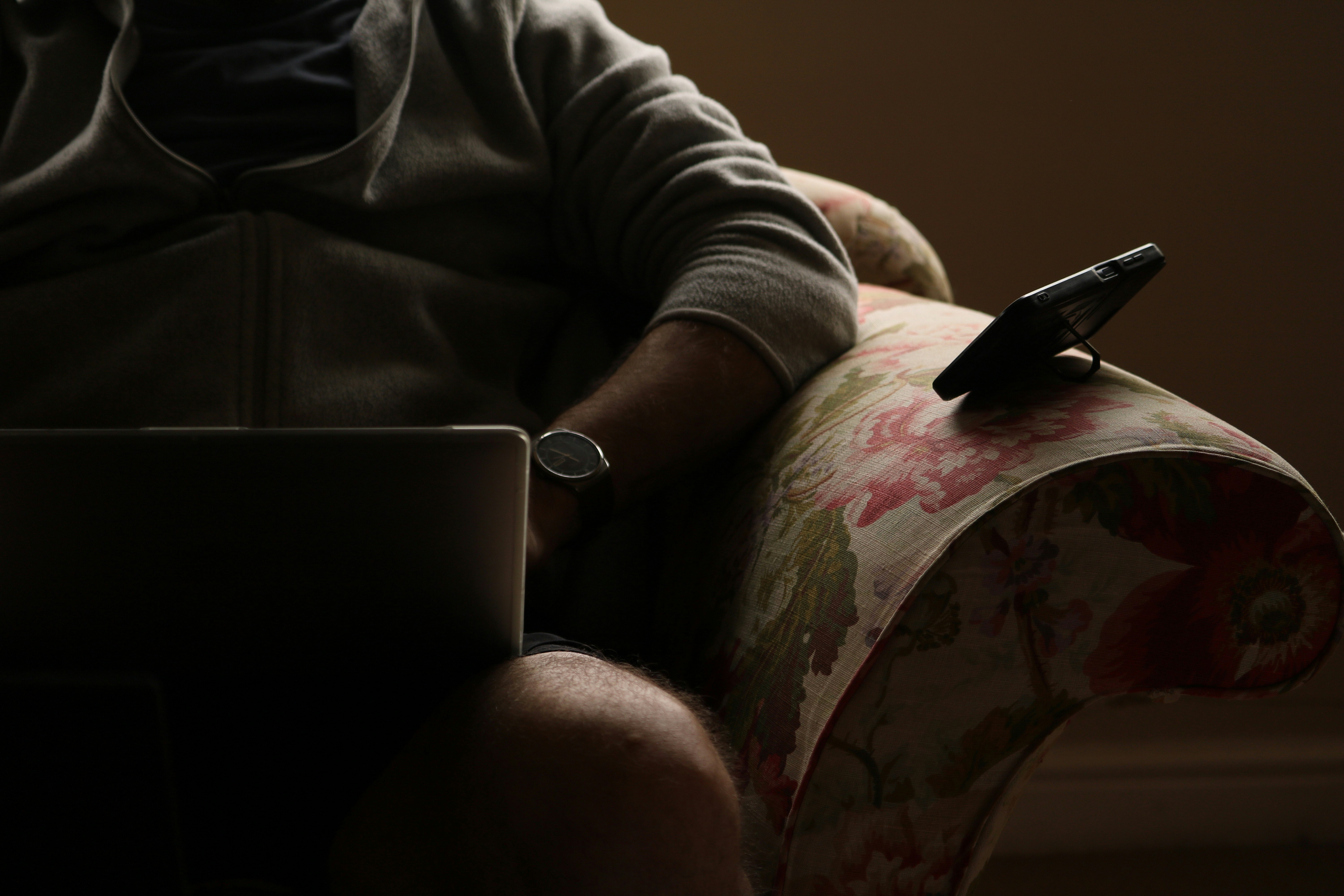 Person sitting in a floral armchair with laptop and phone.
