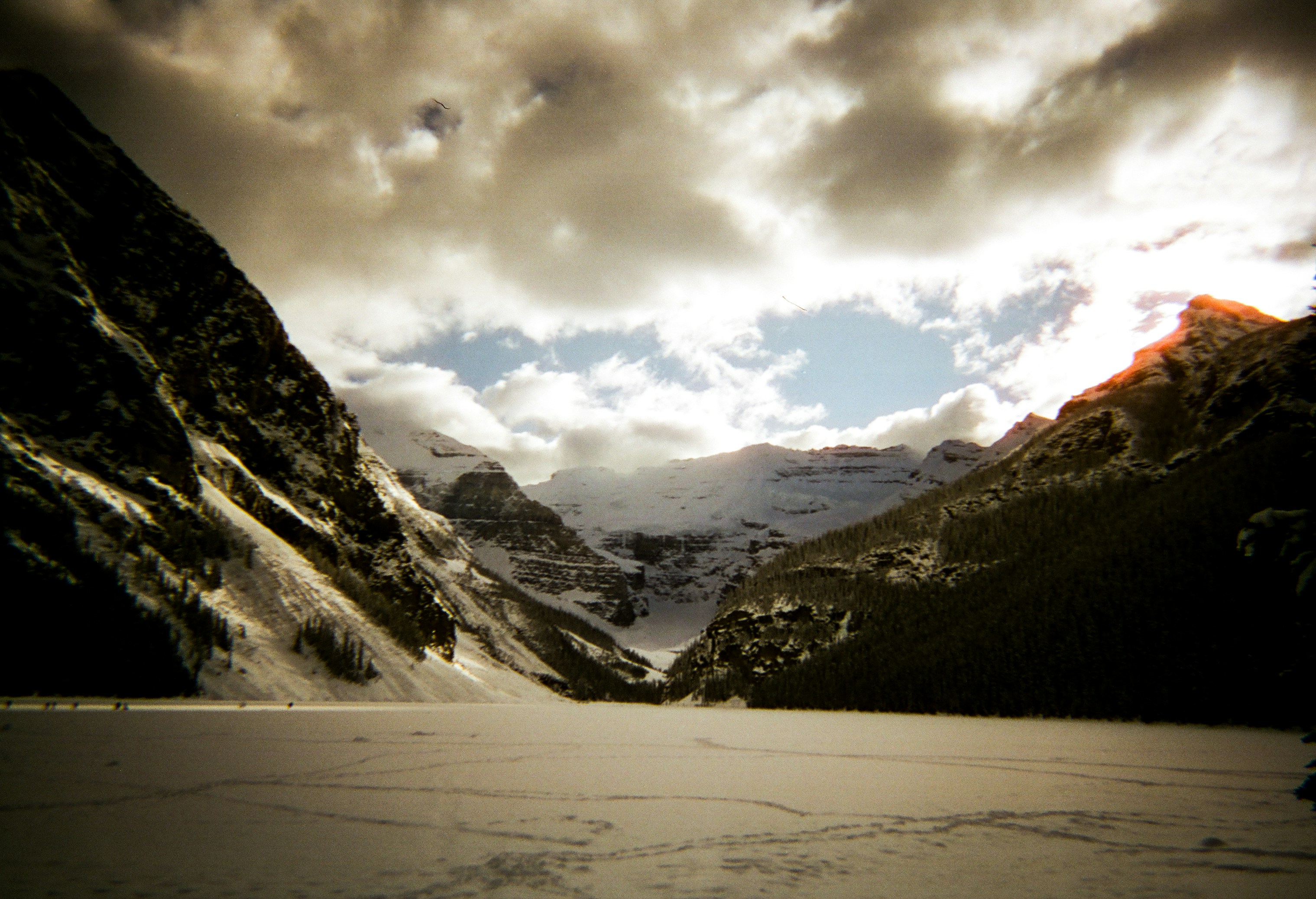 Snowy mountains and frozen lake under dramatic clouds