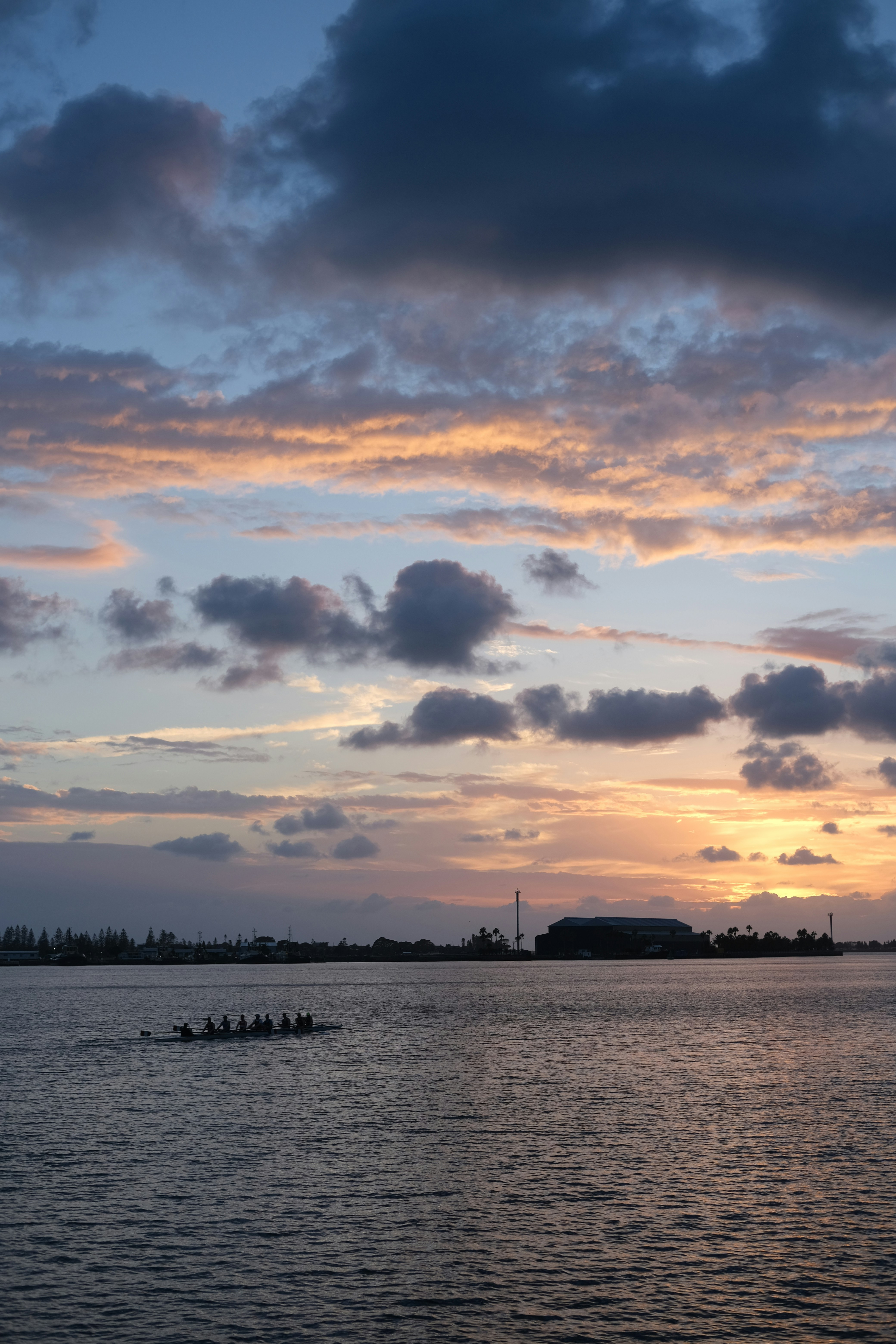 Dragon boat team rows across calm water at sunset
