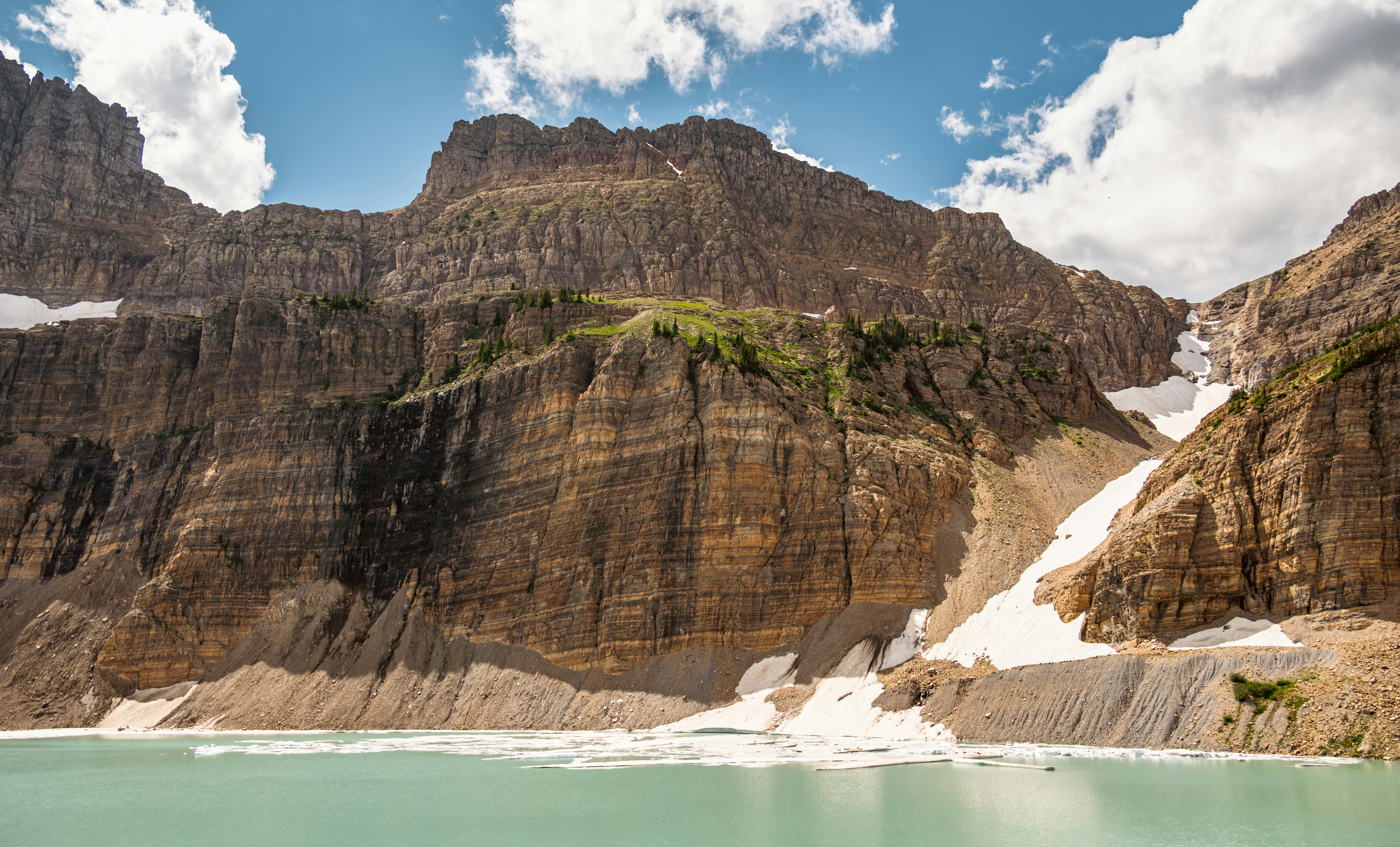 Jagged mountains rise above a turquoise lake with snow patches.