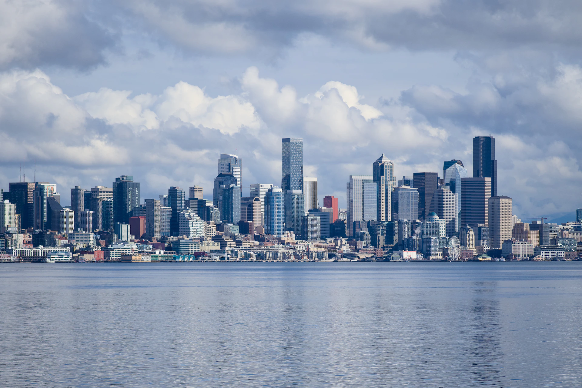 City skyline reflected in calm water under cloudy sky.