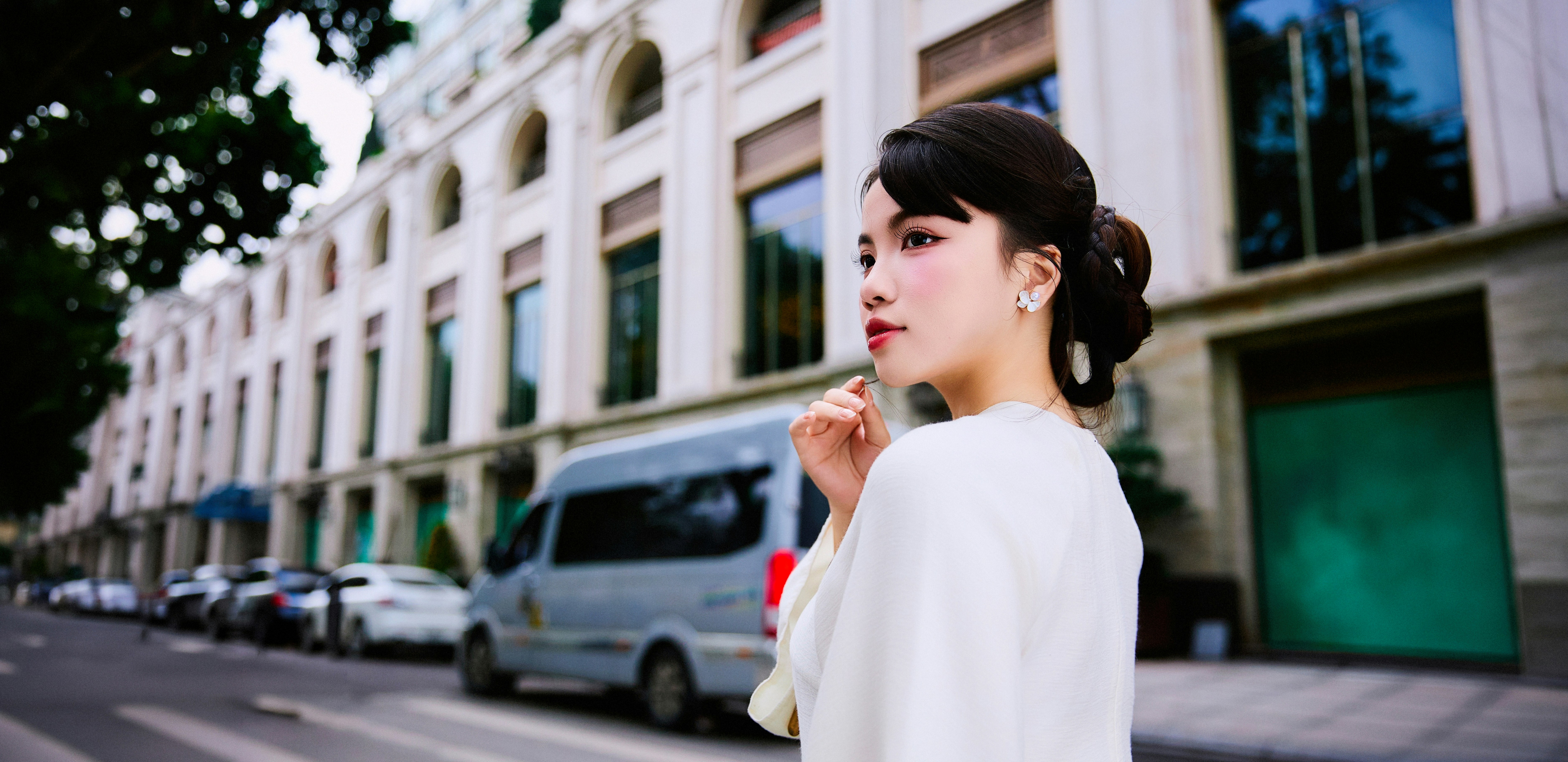 Woman in white dress standing on street with buildings behind.