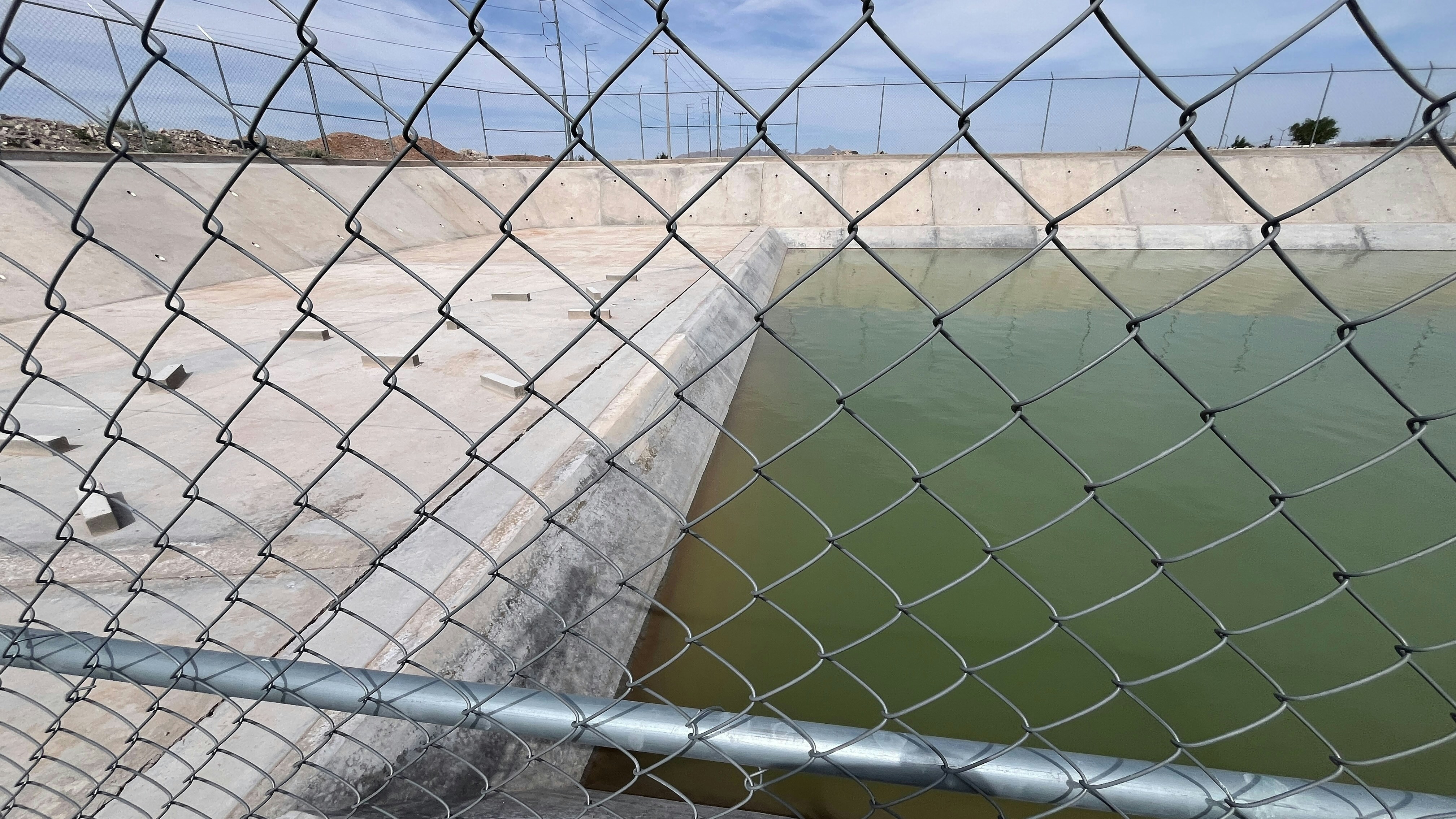 Betonreservoir mit grünem Wasser hinter Zaun