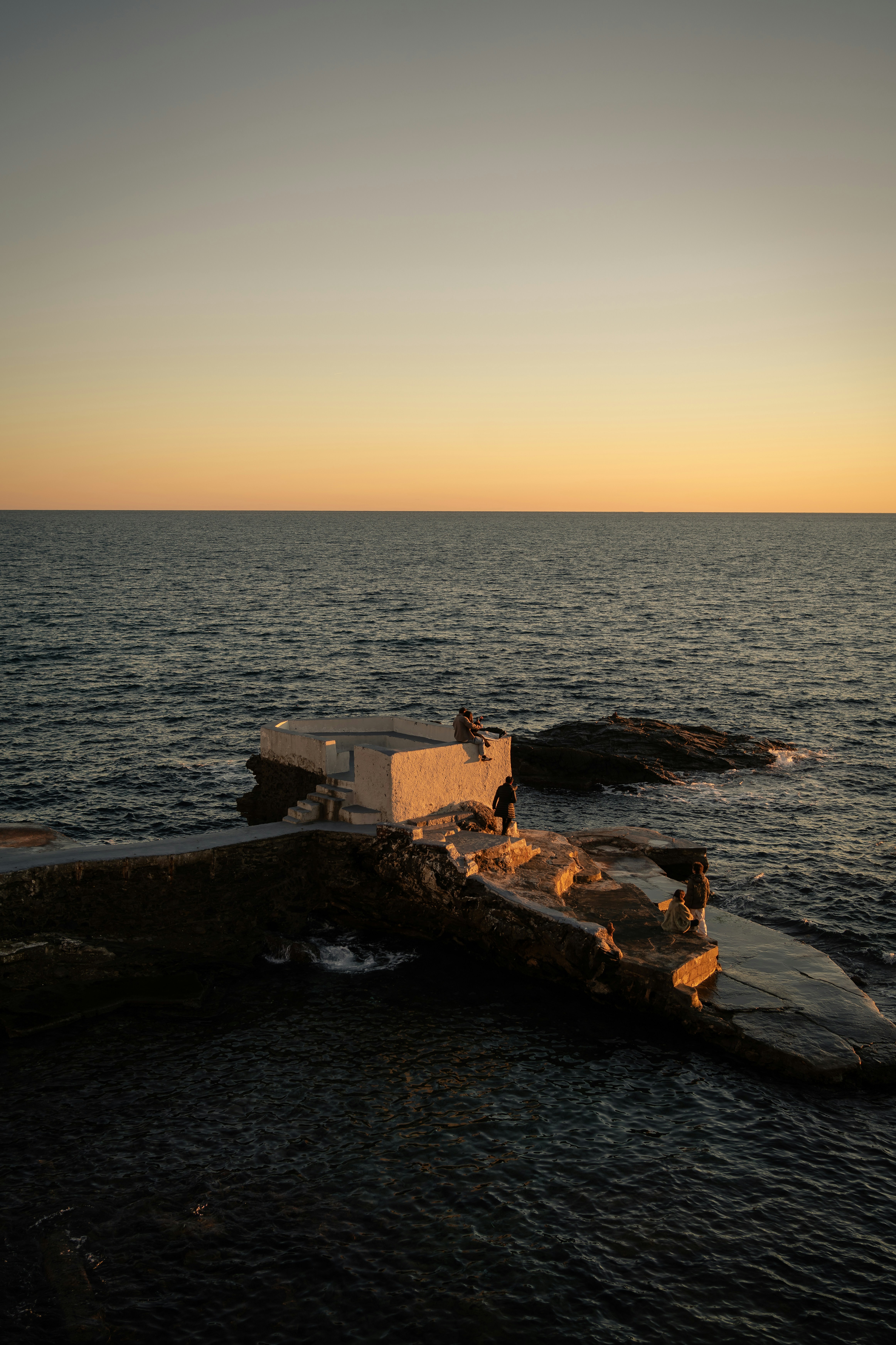 People on concrete structure by the ocean at sunset