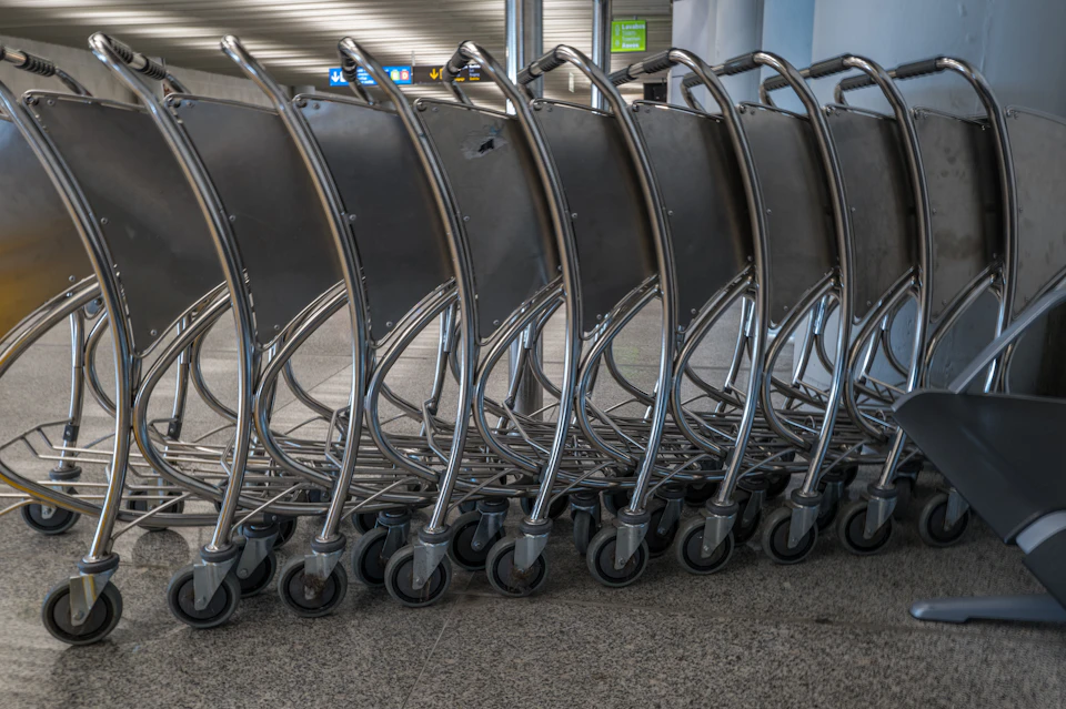 Row of silver luggage carts line up against gray wall with empty interior spaces