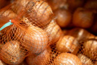 Onions in orange netting bags stacked together.