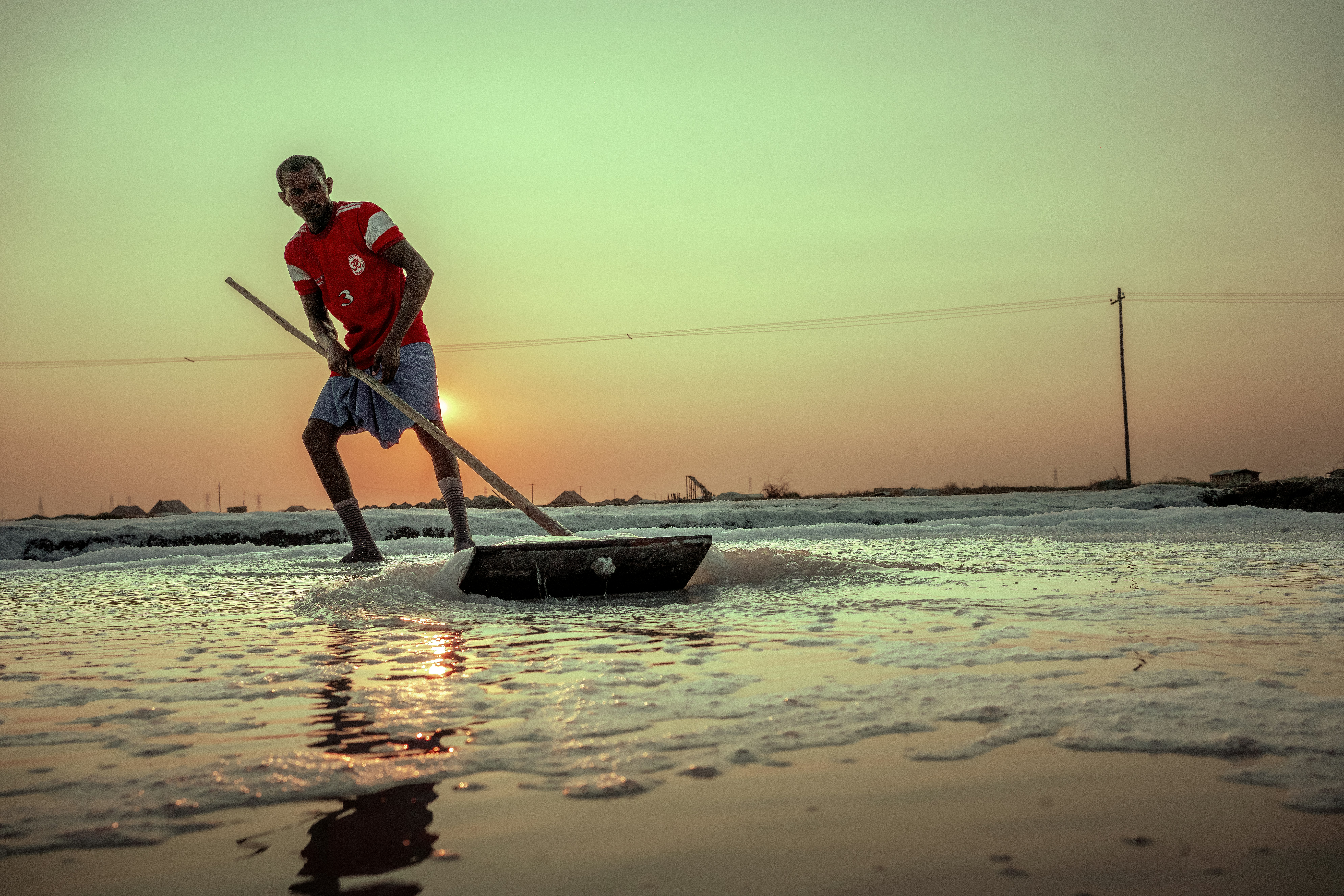 Man raking salt at sunset on a salt flat.