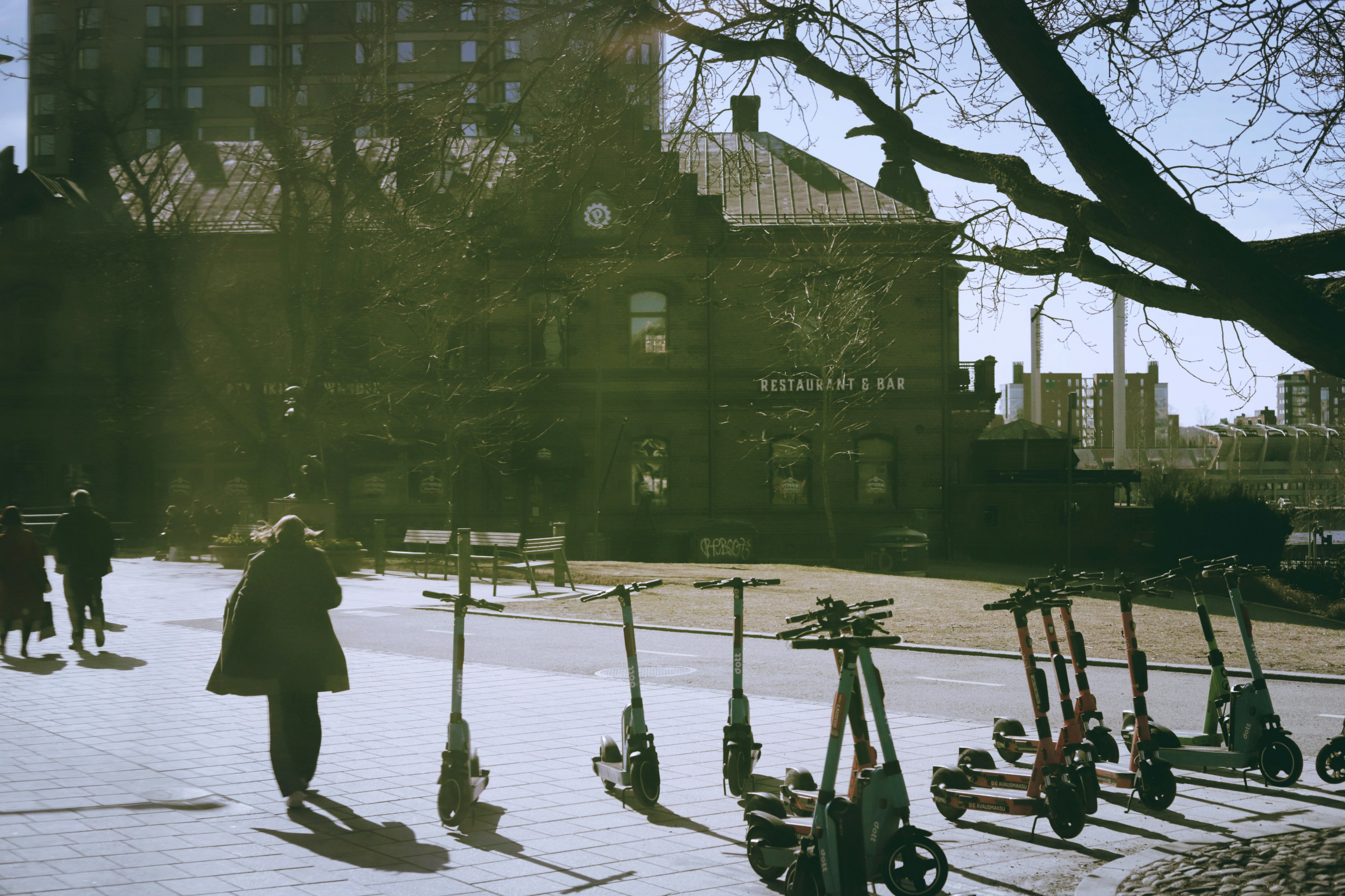 Electric scooters lined up on sidewalk with people walking.