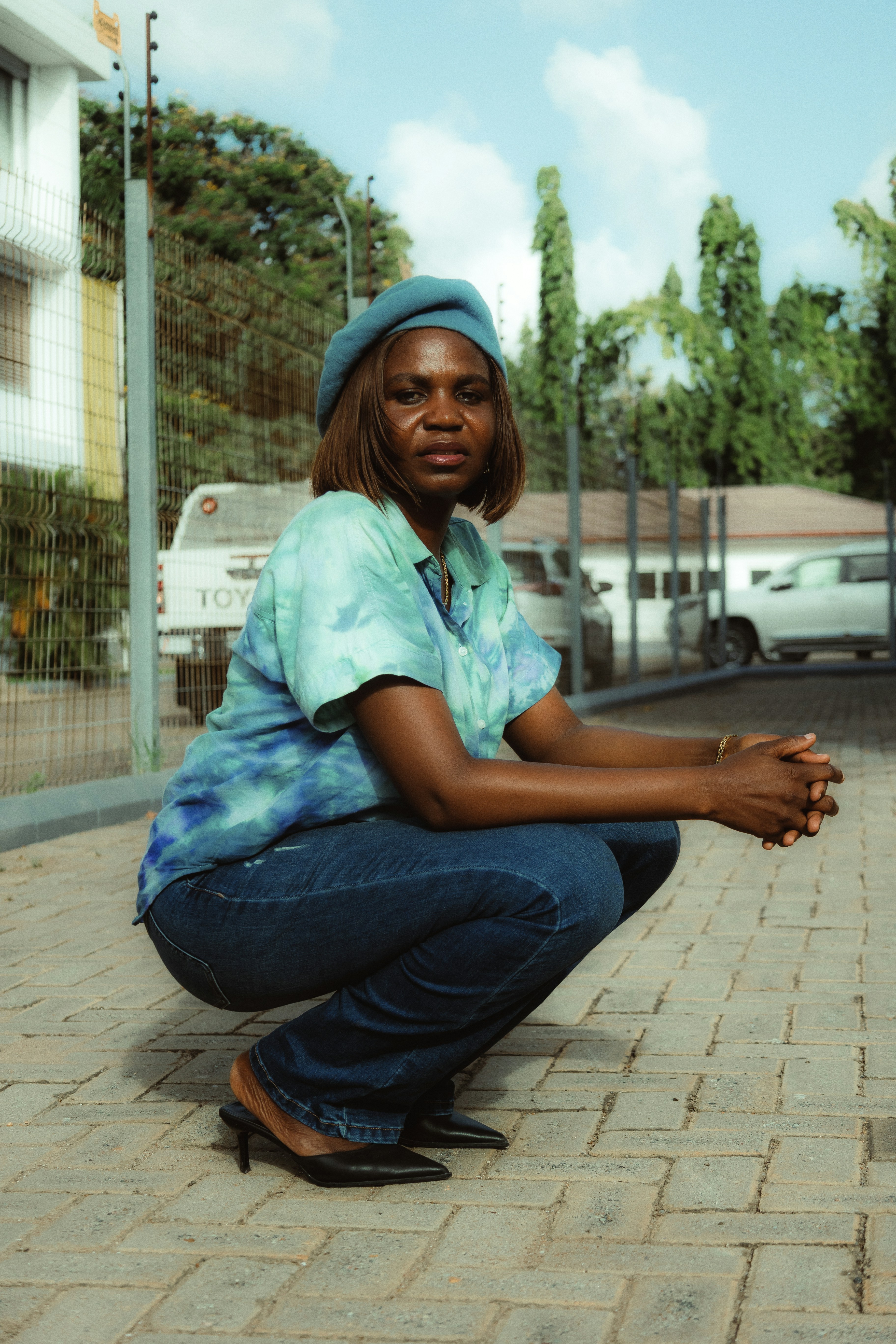 A woman in a blue beret squats outdoors.