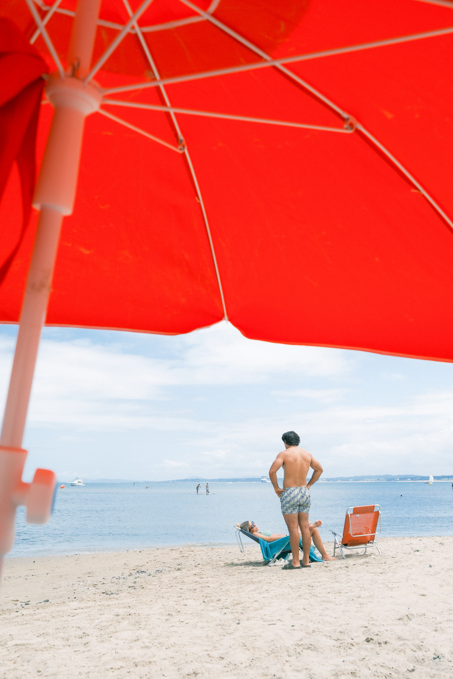 People relaxing beneath a red beach umbrella beside the ocean