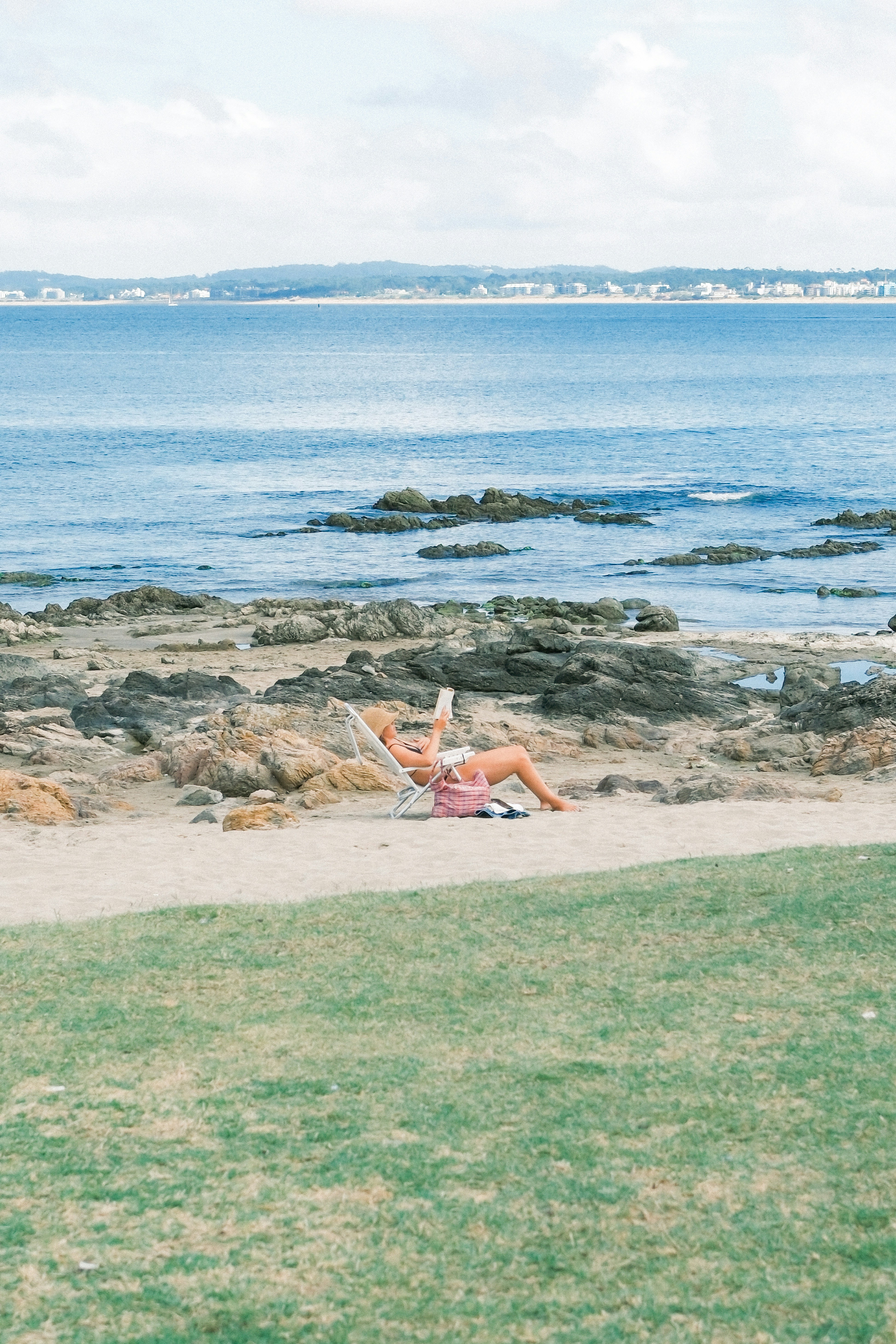 Woman reading on a rocky beach by the ocean.