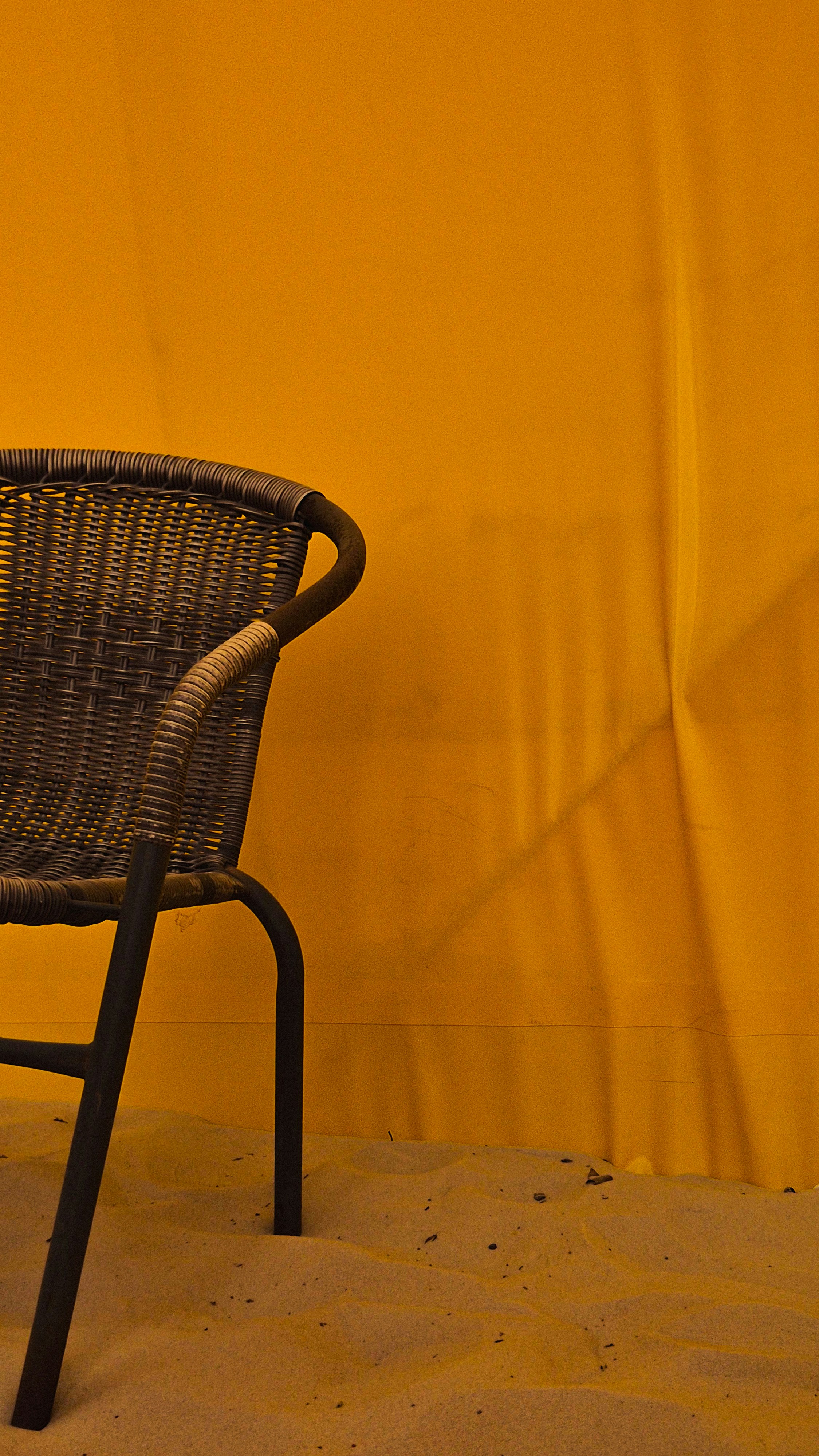 Wicker chair on sand against yellow background.
