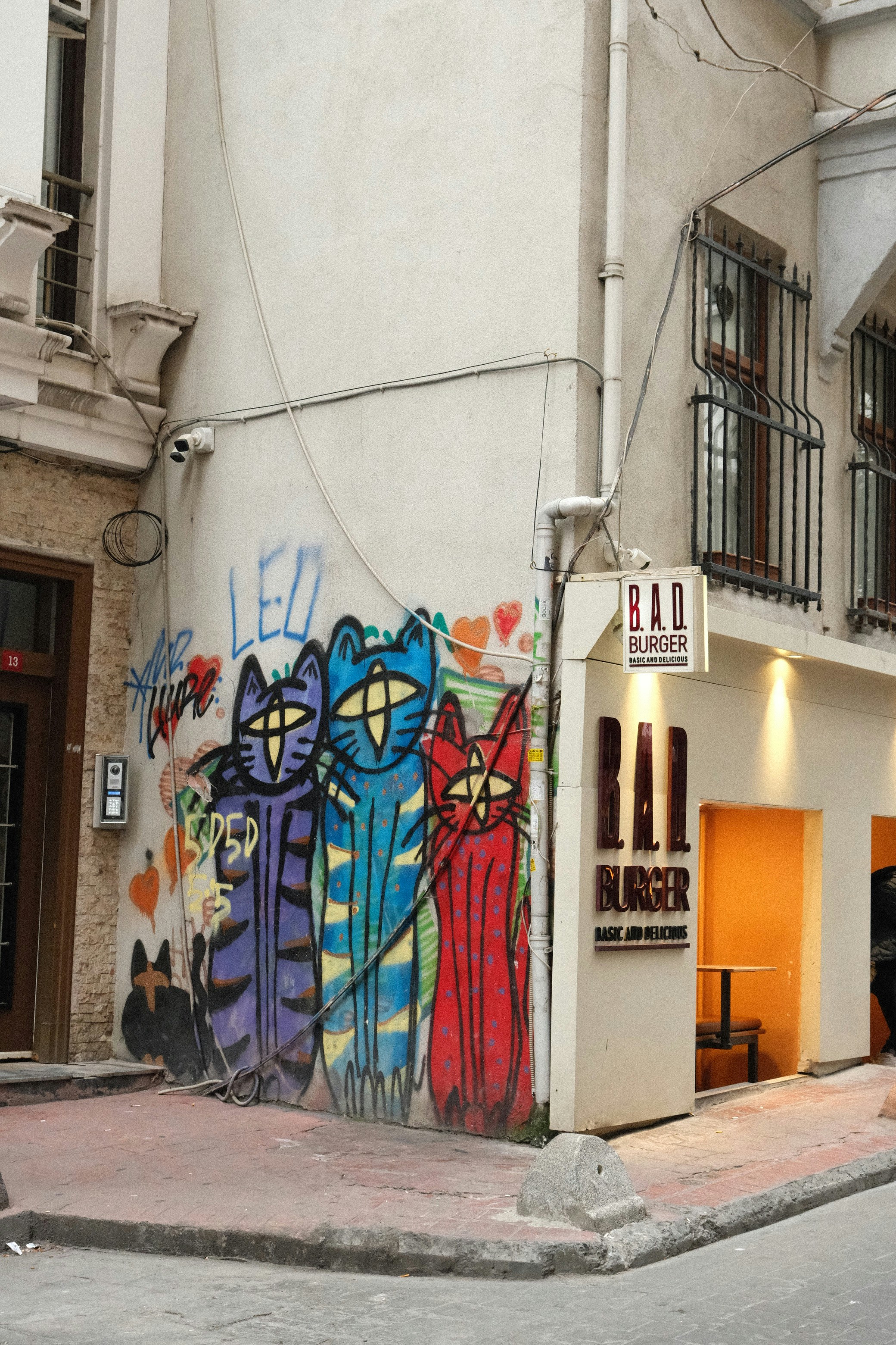 Graffiti von drei bunten Katzen an einer Gebäudewand.
