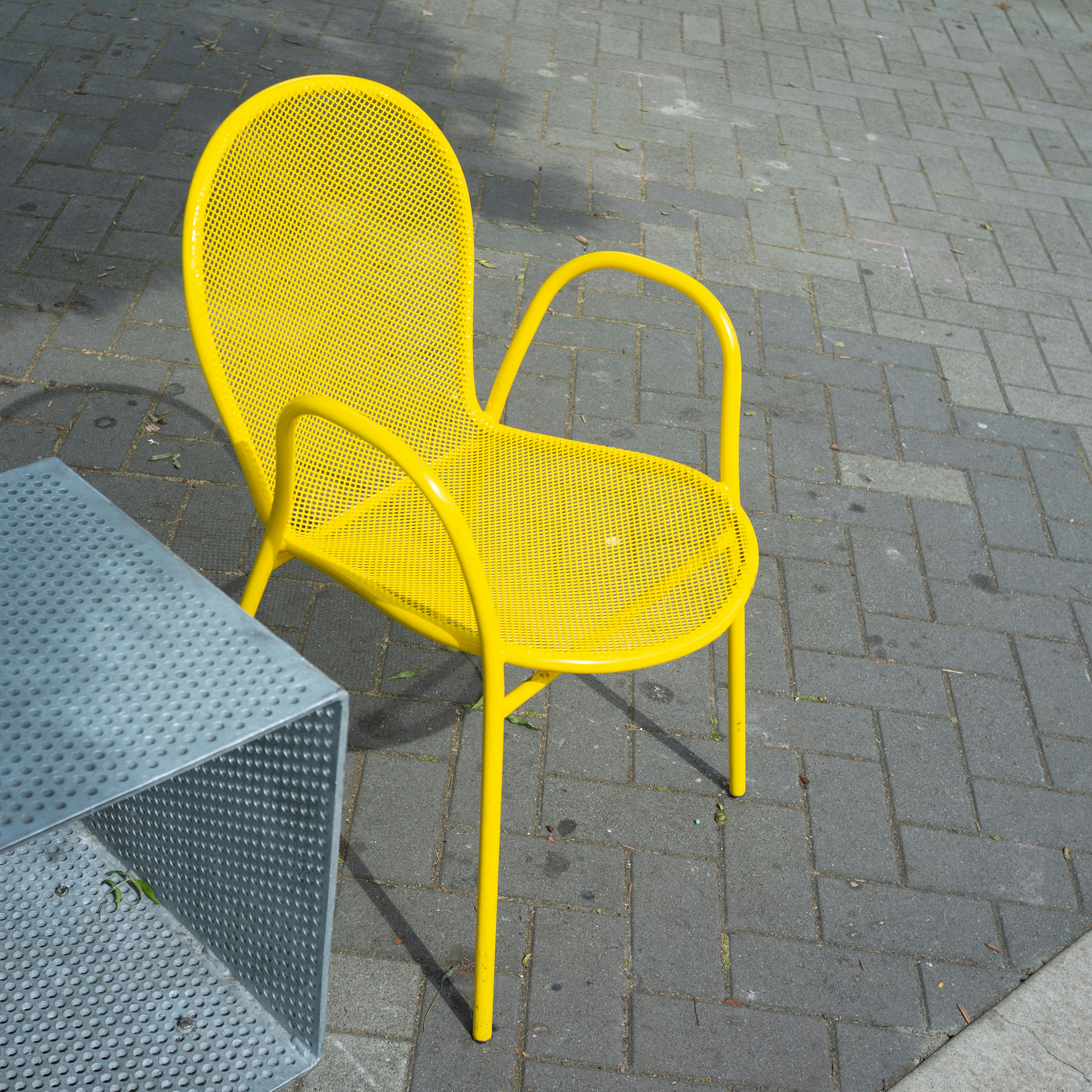 A bright yellow chair sits on a paved surface.