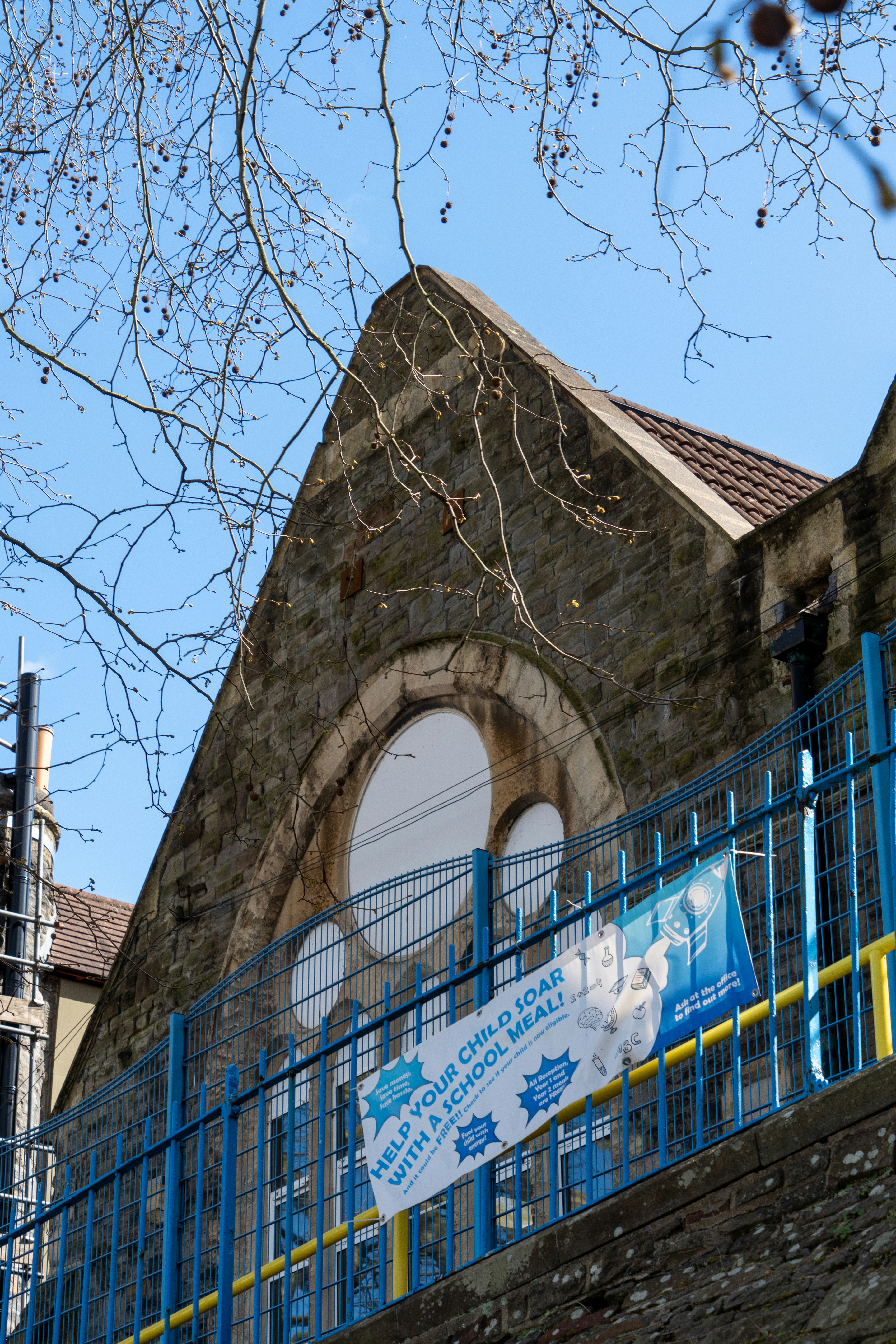 Edificio in pietra con recinzione blu e striscione per la mensa scolastica.