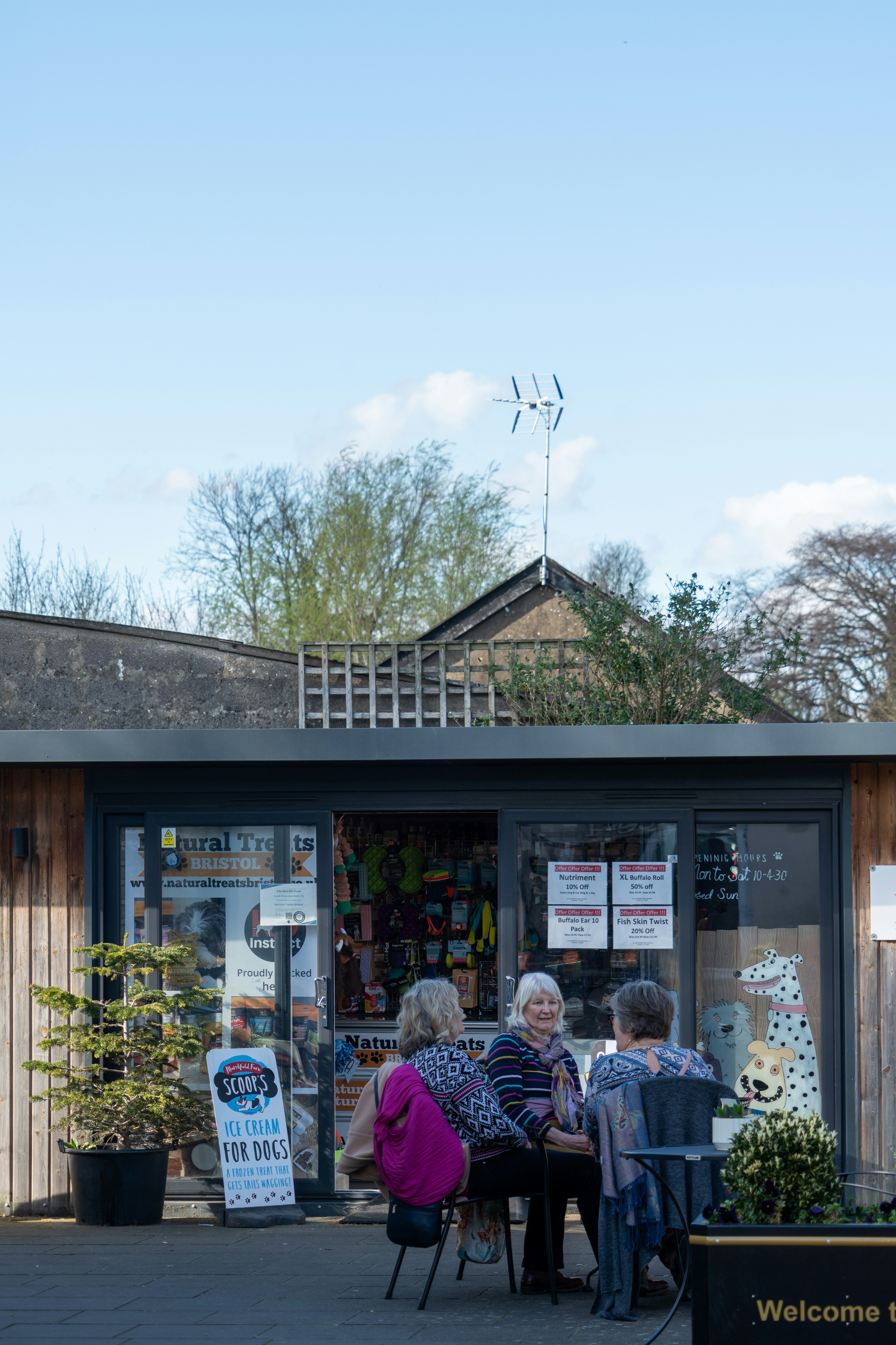 Three women sitting at a table outside a shop.