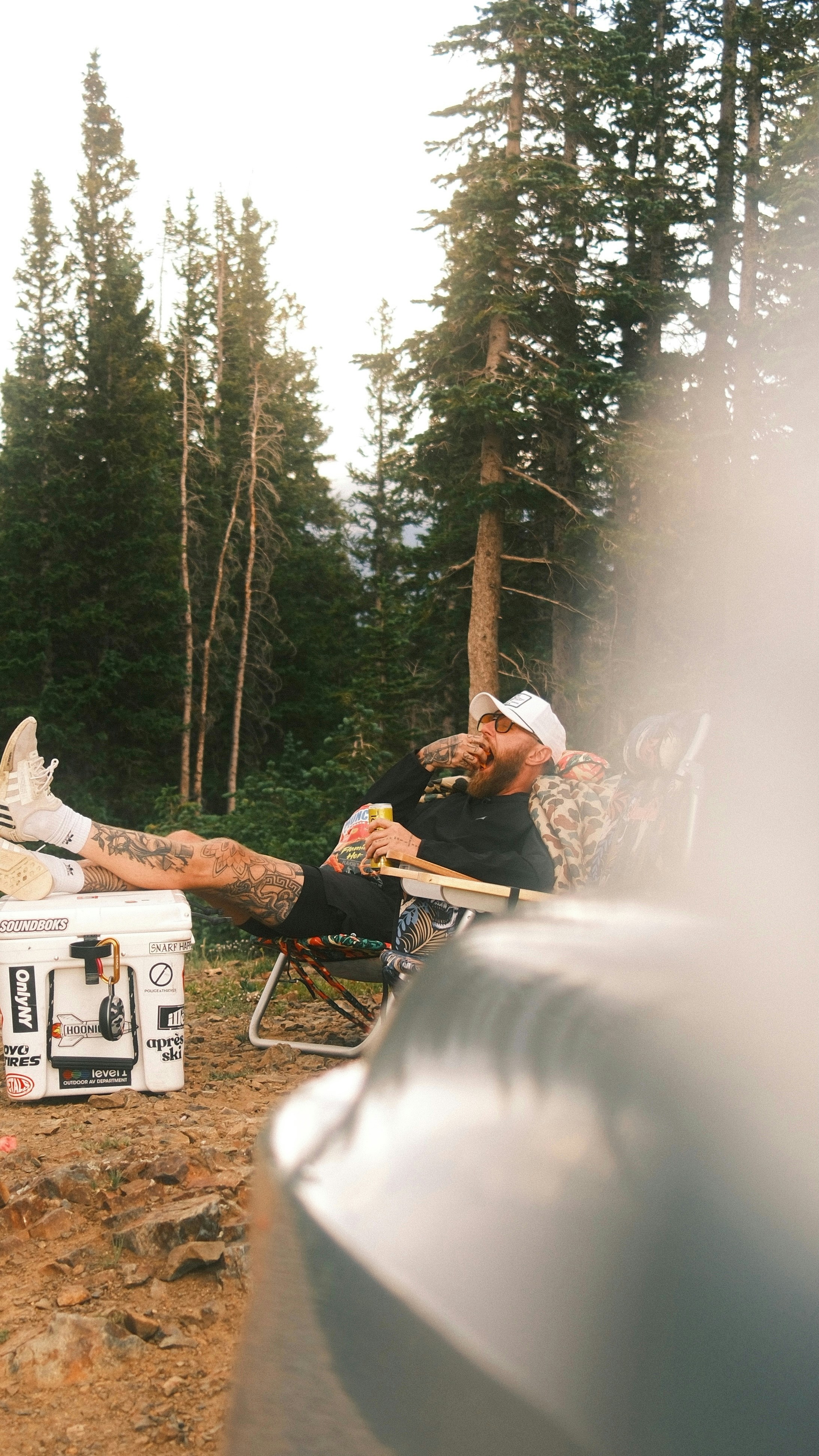 Pria bersantai di kursi berkemah minum minuman.