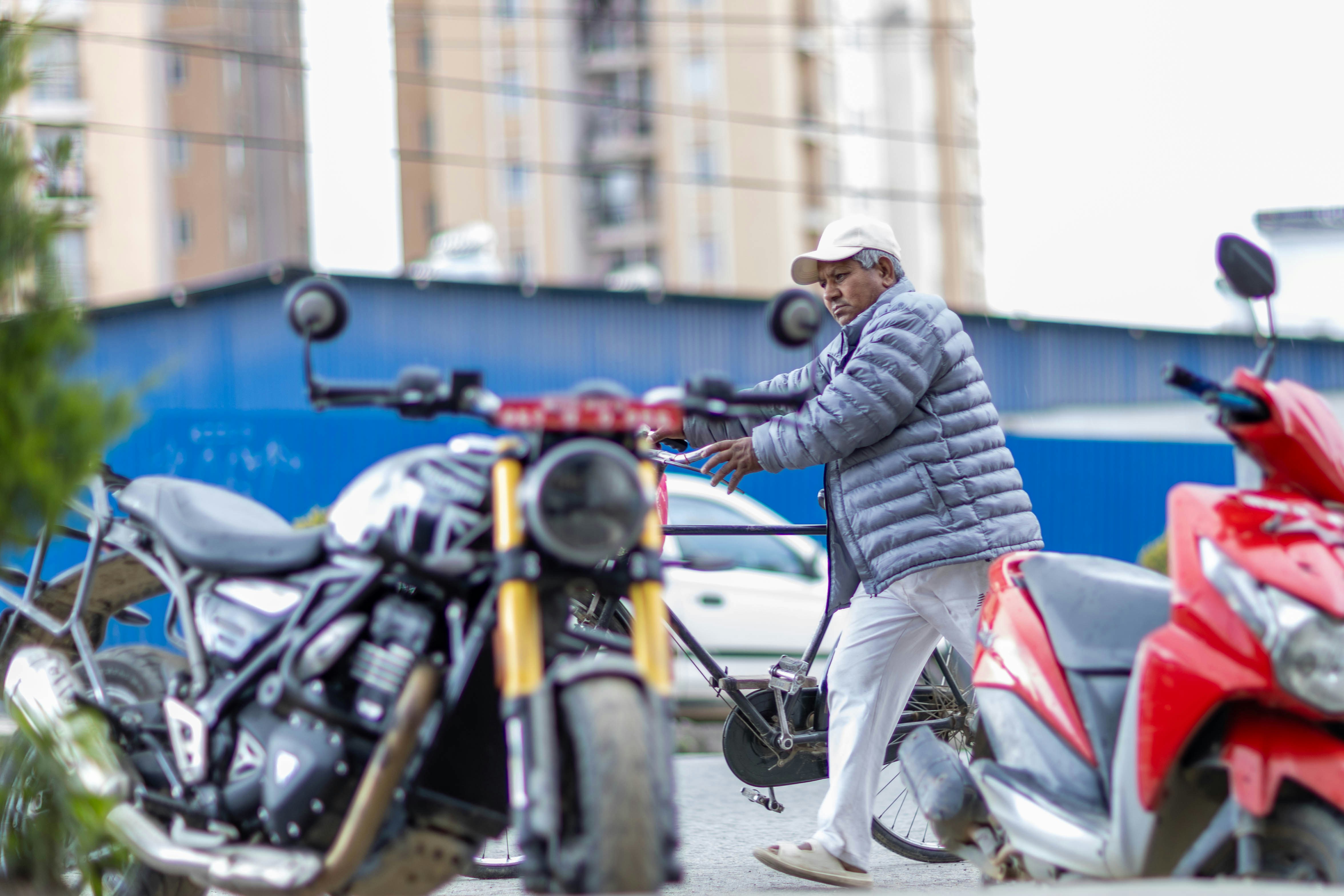 ジャケットと帽子をかぶった高齢の男性がバイクの近くにいる