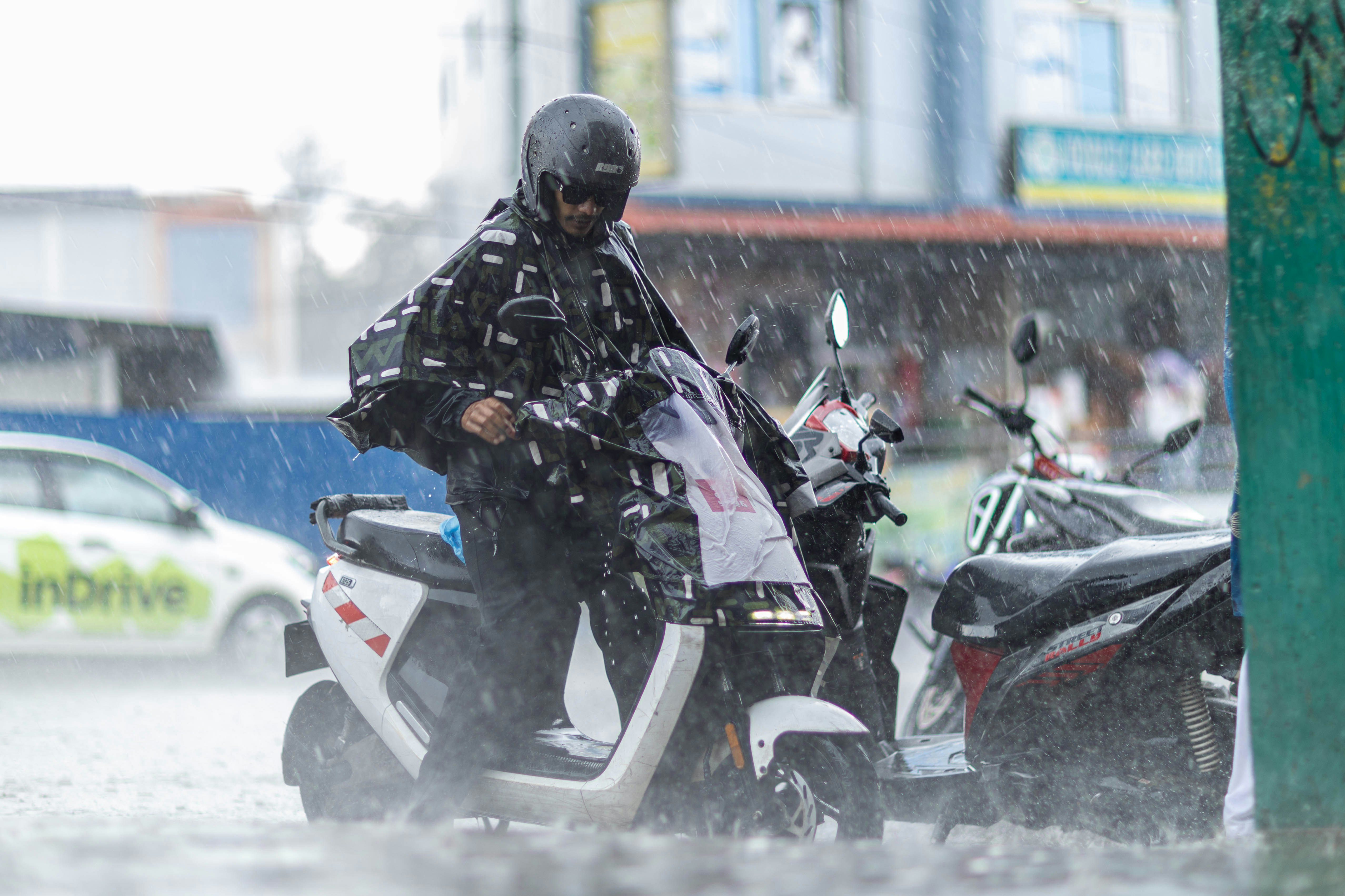 雨具を着た人が大雨の中スクーターに乗っている。